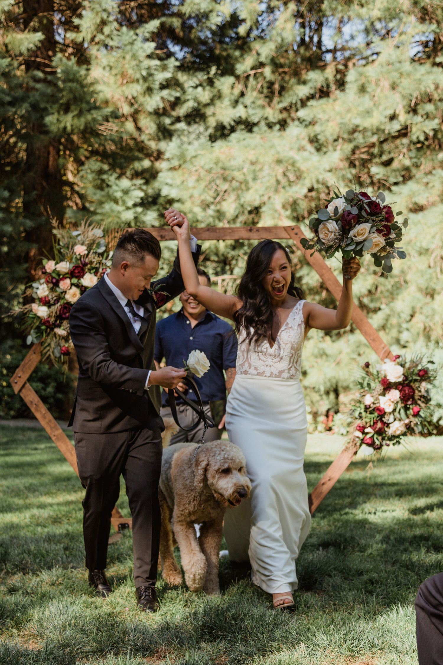 Wedding celebration with a couple and their dog under a hexagonal arch decorated with flowers.