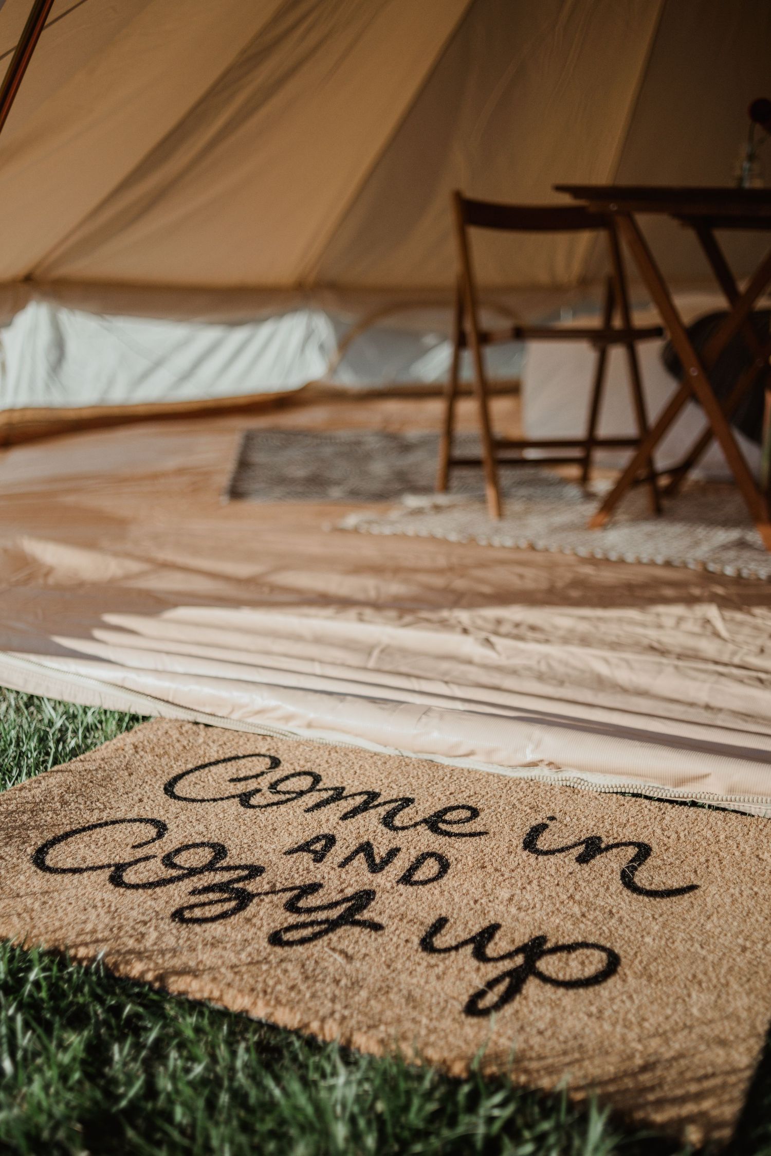 A doormat reading 'Come in and cozy up' at the entrance of a white canvas tent.