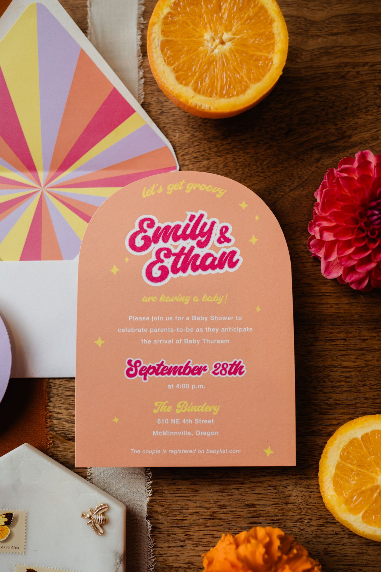 Wedding invitation featuring retro-style text and sunburst envelope liner, styled with citrus and flowers.