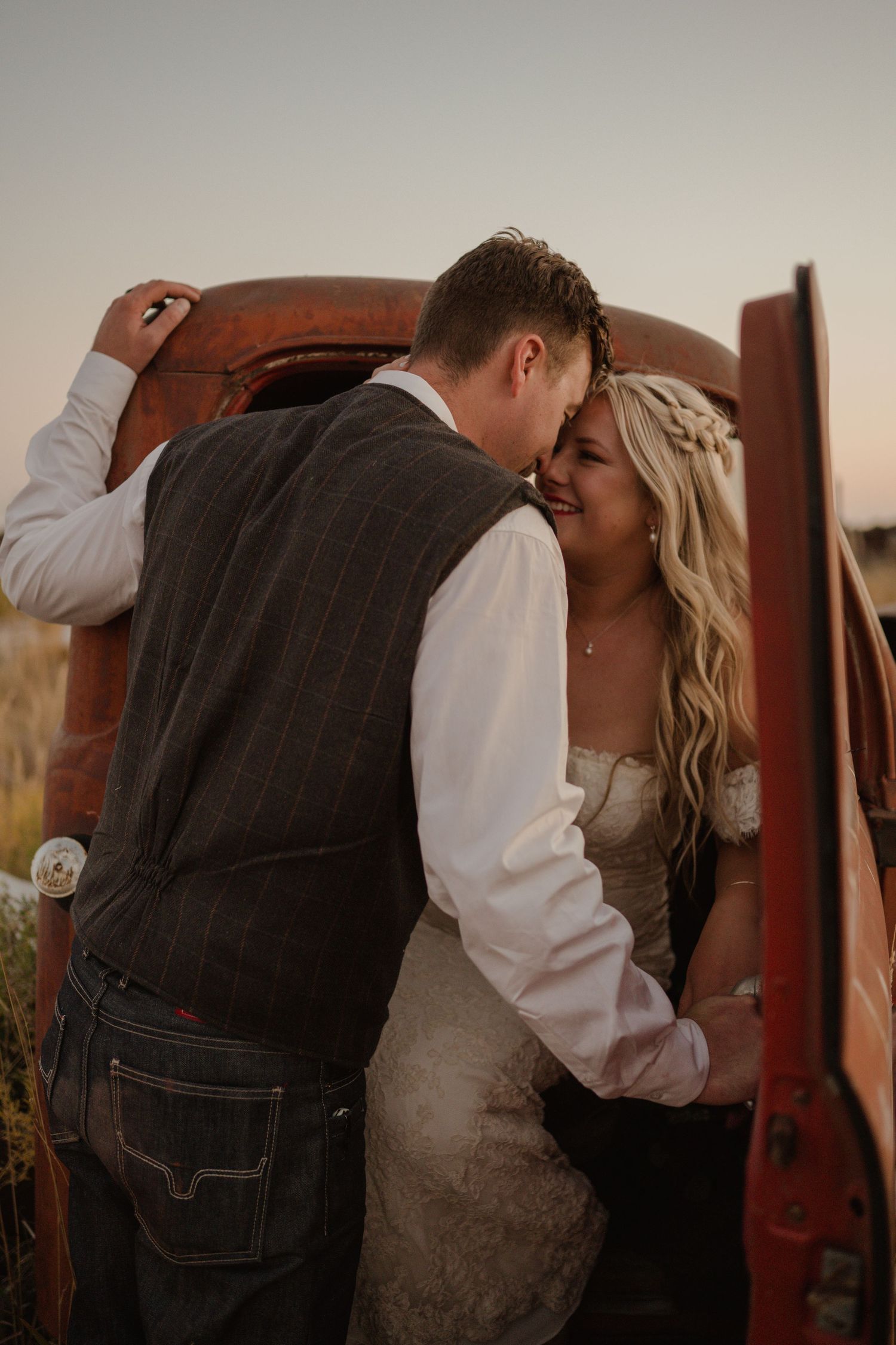 Intimate wedding moment captured against a vintage red truck at golden hour.