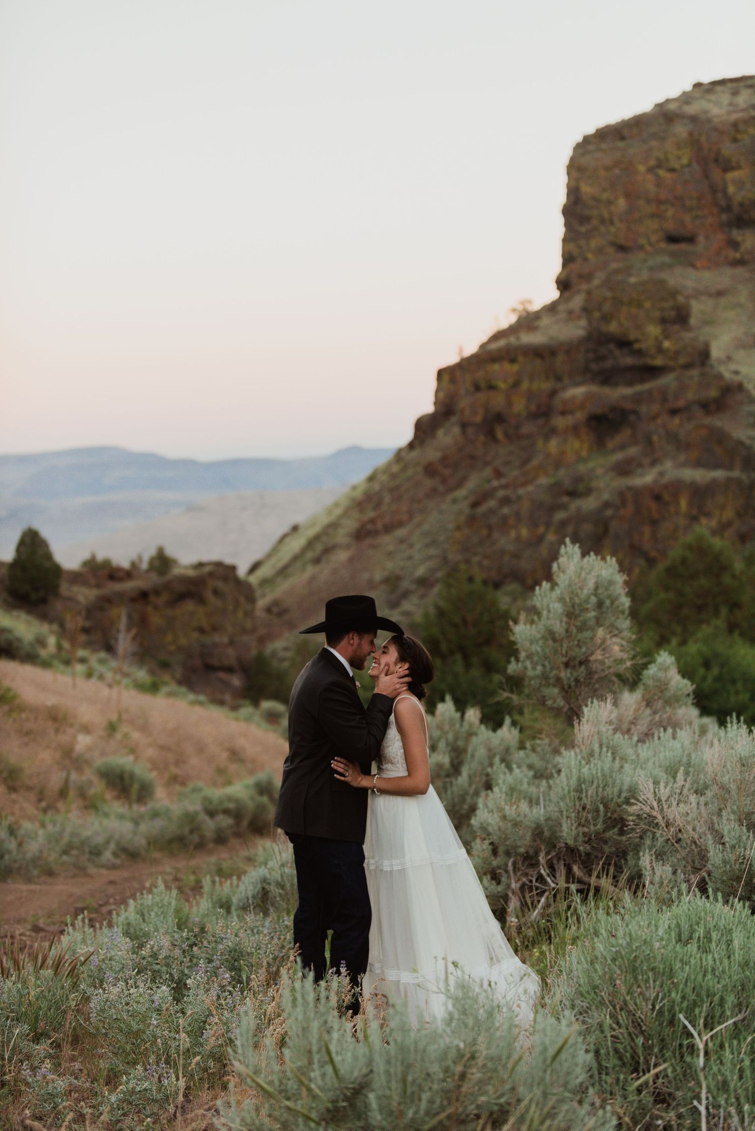 A romantic wedding moment against rugged cliffs and sagebrush at dusk.