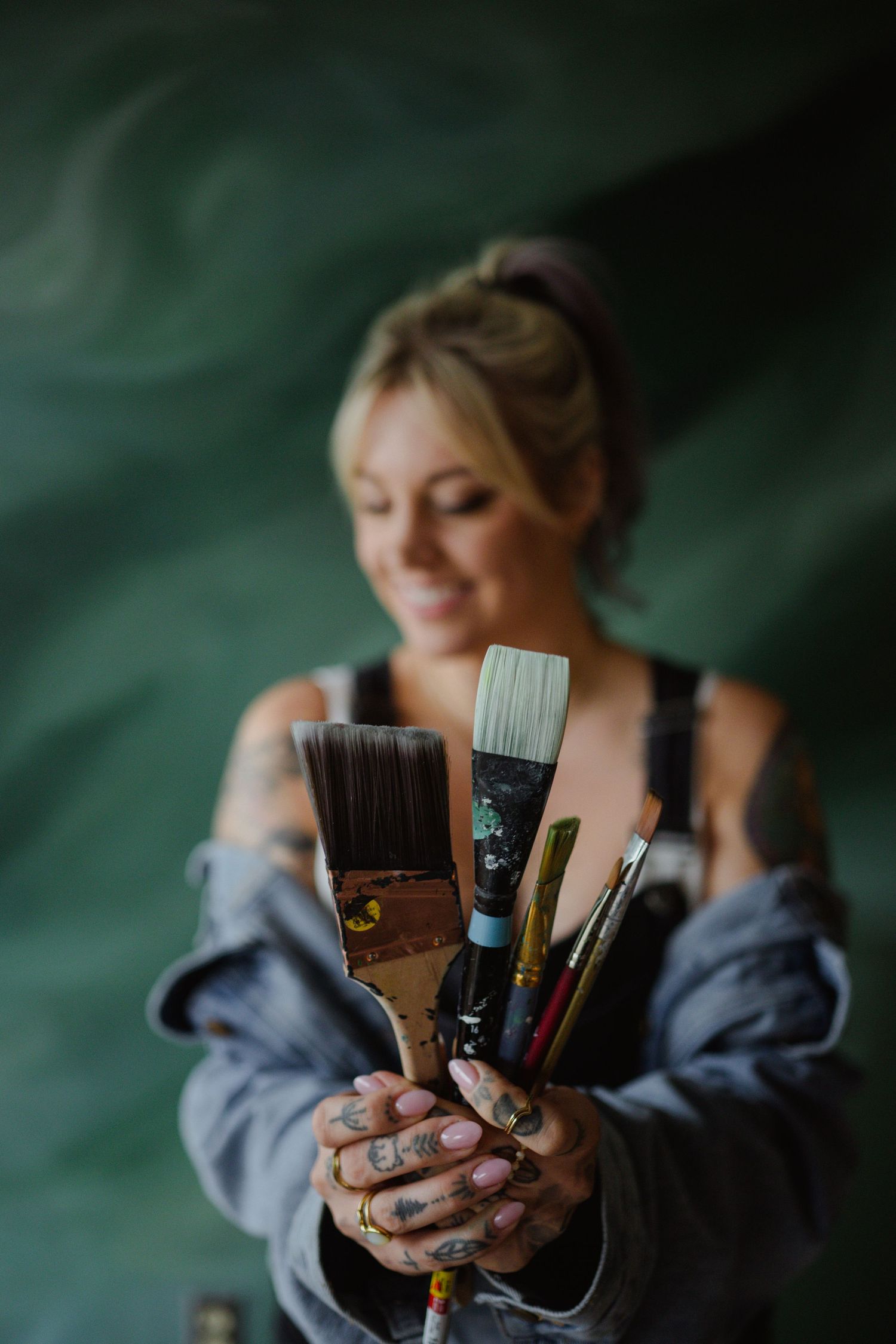 Artist holding a collection of paint brushes against a dark green background.