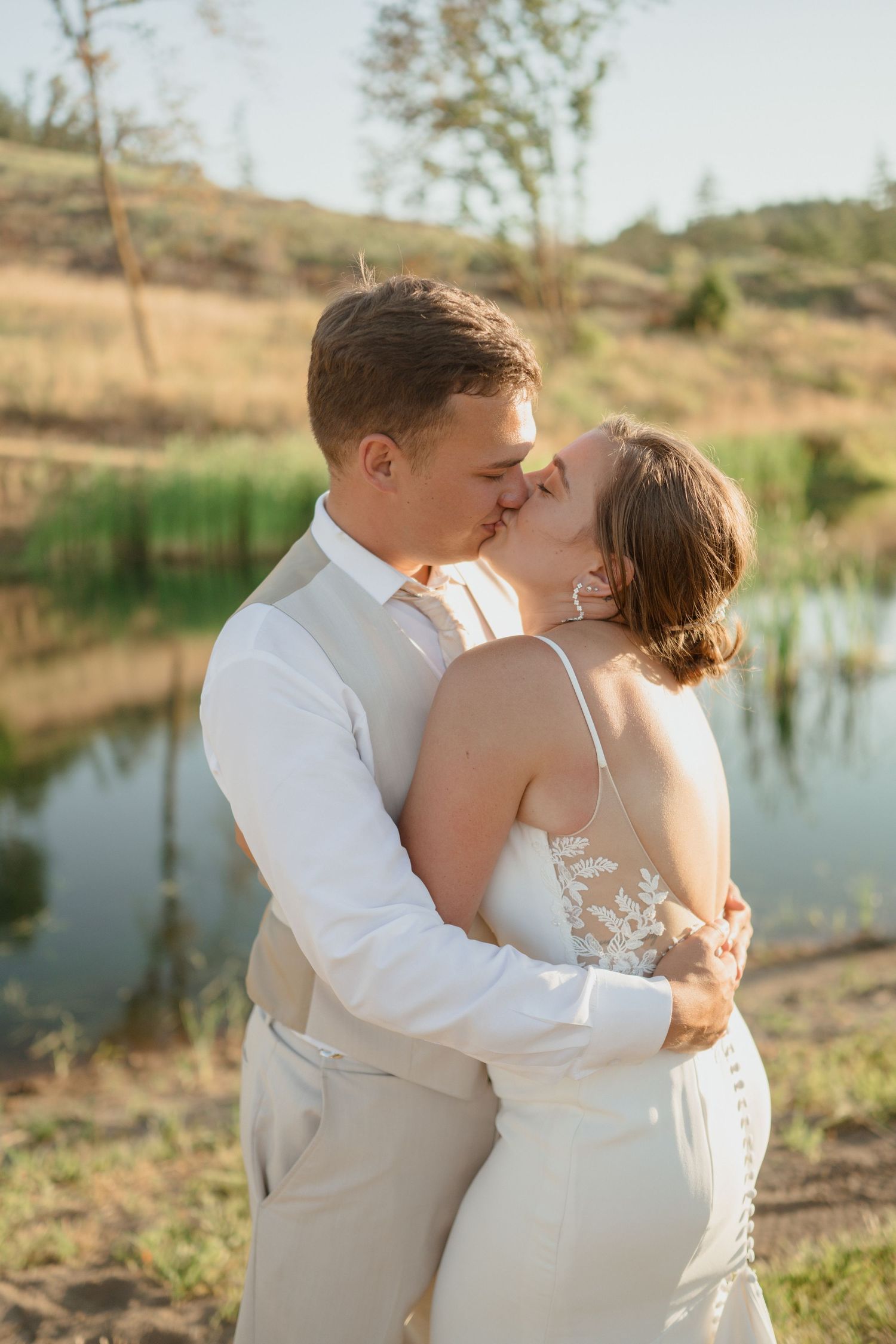 A romantic moment between newlyweds near a pond at sunset.