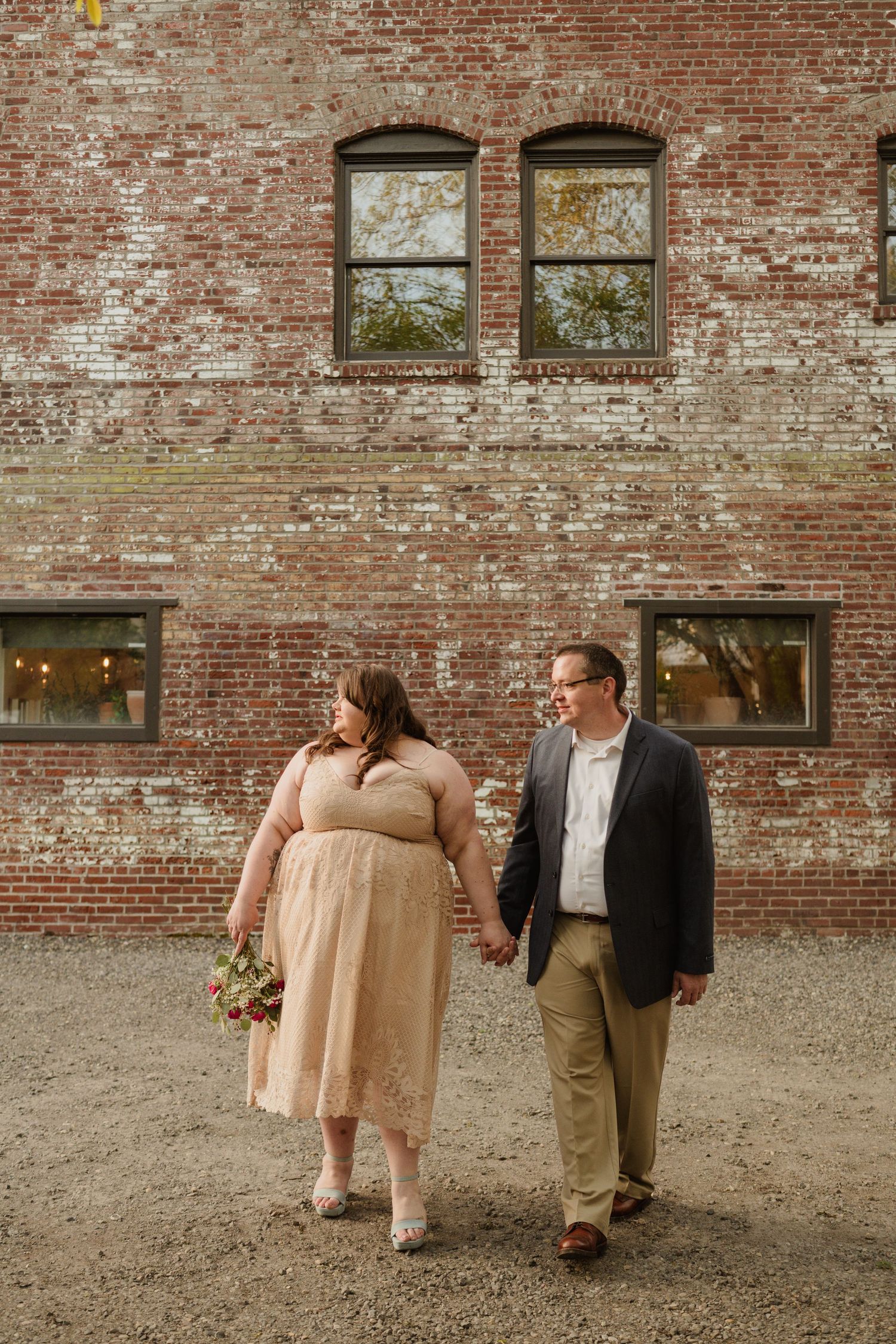 A couple poses against a rustic brick wall with vintage windows during their wedding day.