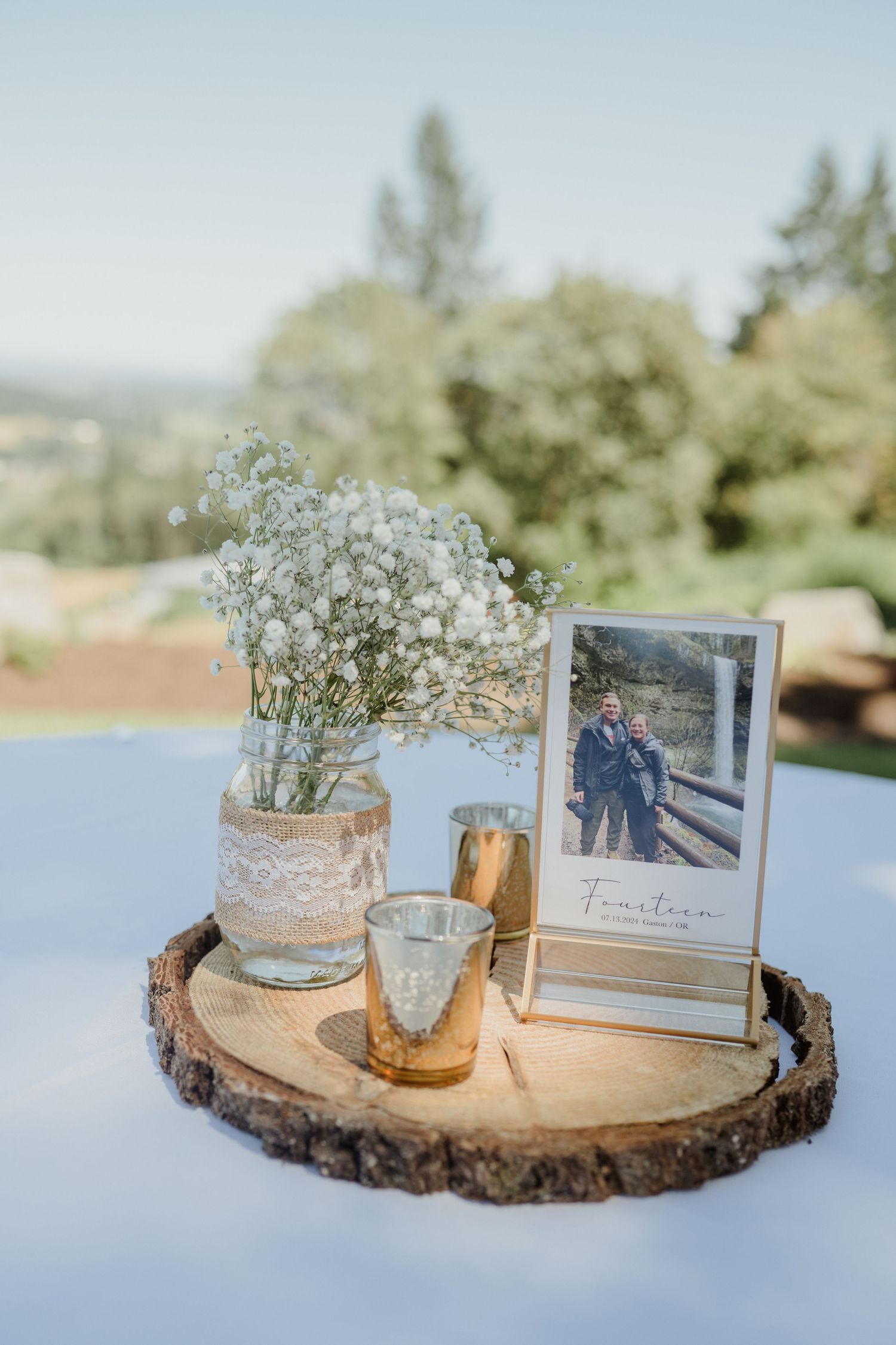 Rustic wedding centerpiece with baby's breath in a mason jar on a wood slice with a framed photo.
