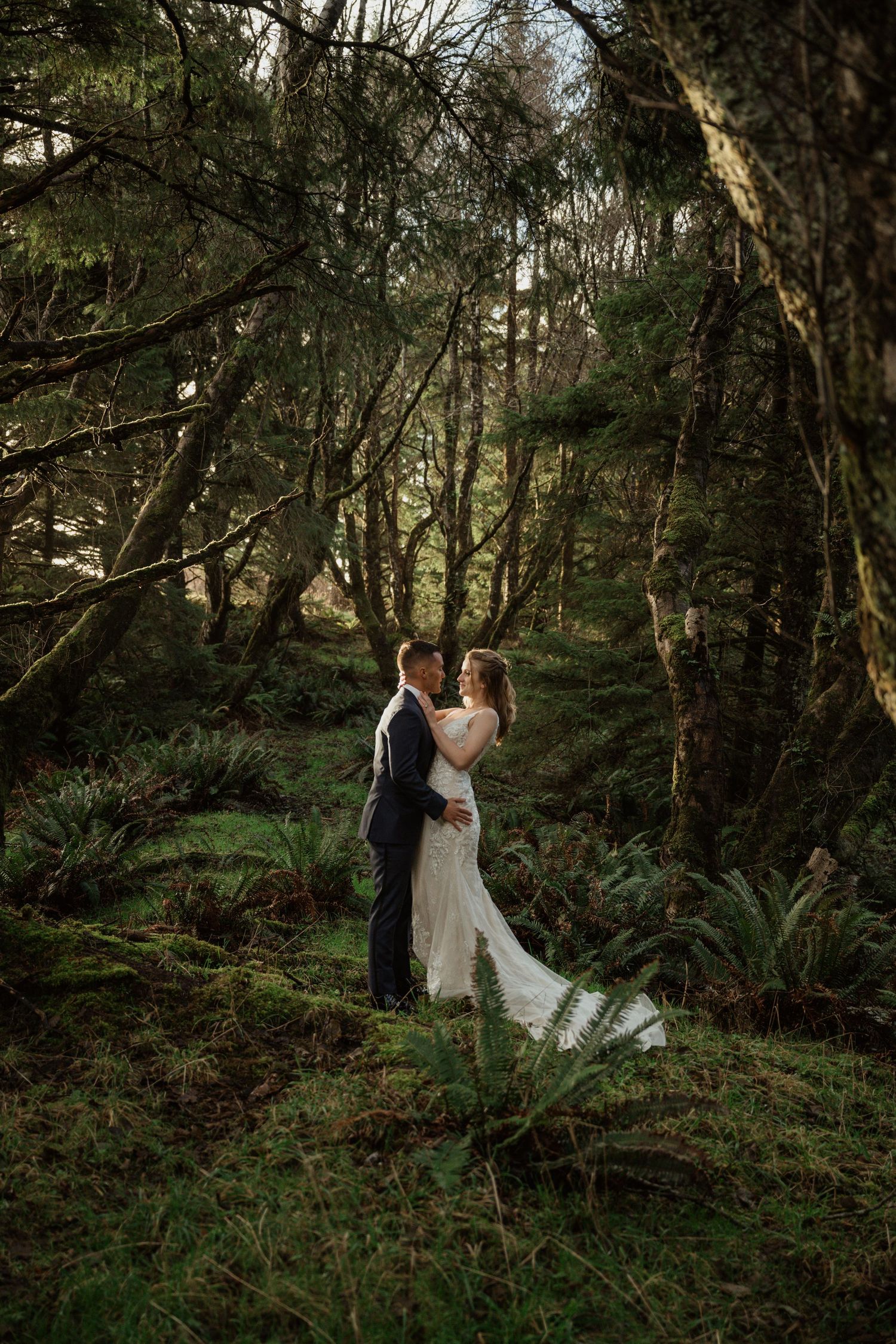 A romantic wedding portrait in a lush, mossy forest setting.