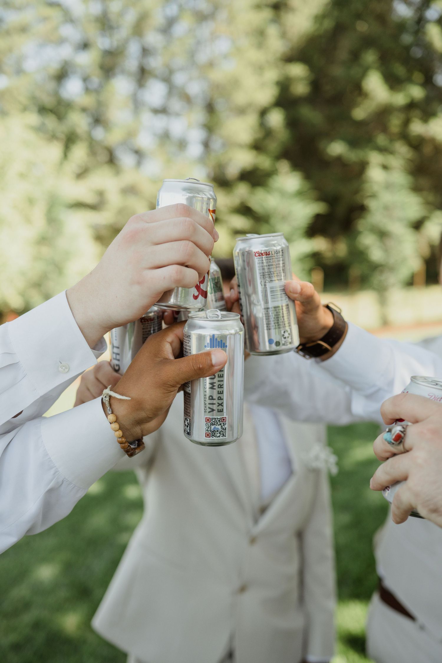 Wedding party members toasting with cans and drinks outdoors.