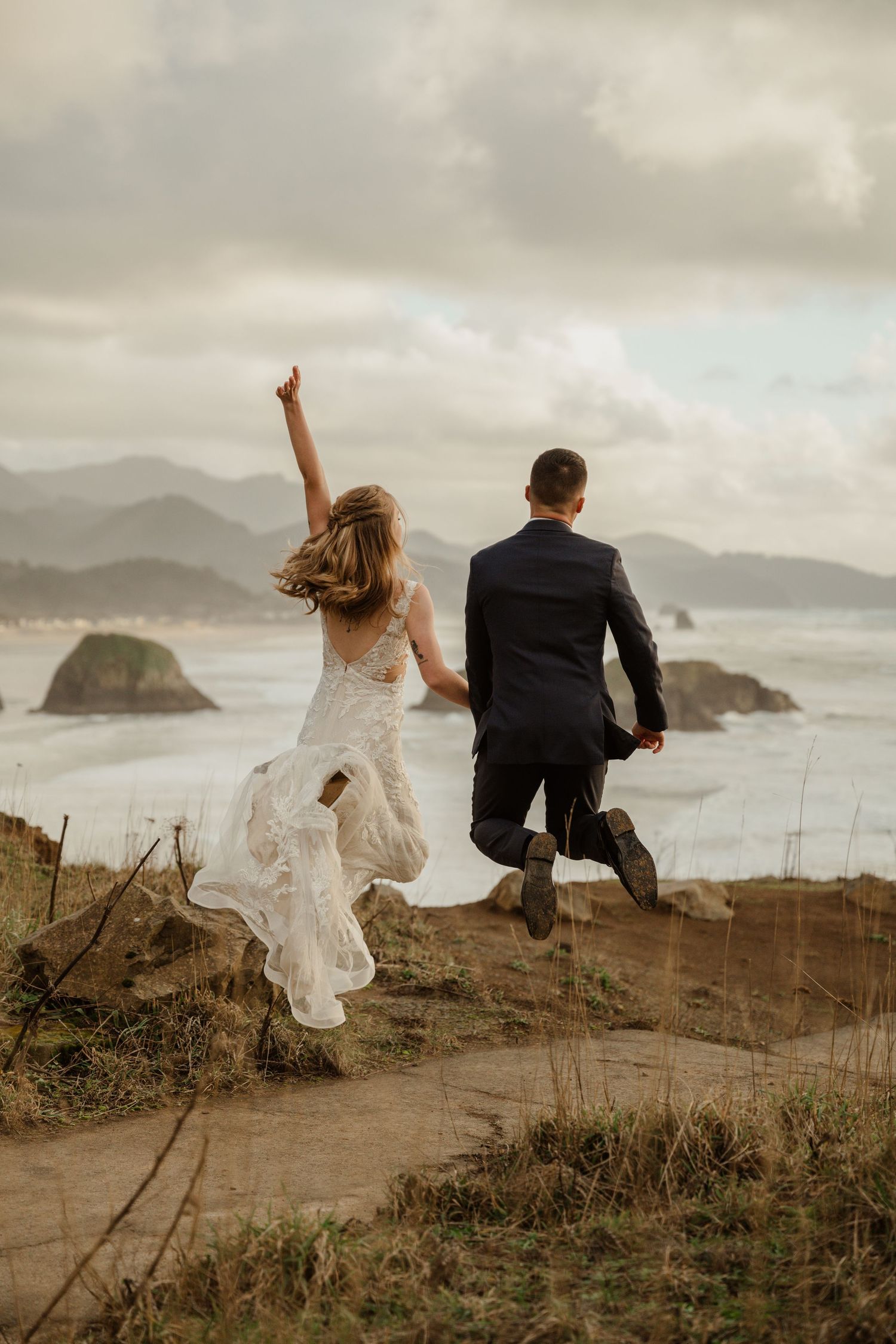 A playful couple runs along a coastal cliff edge with ocean views.