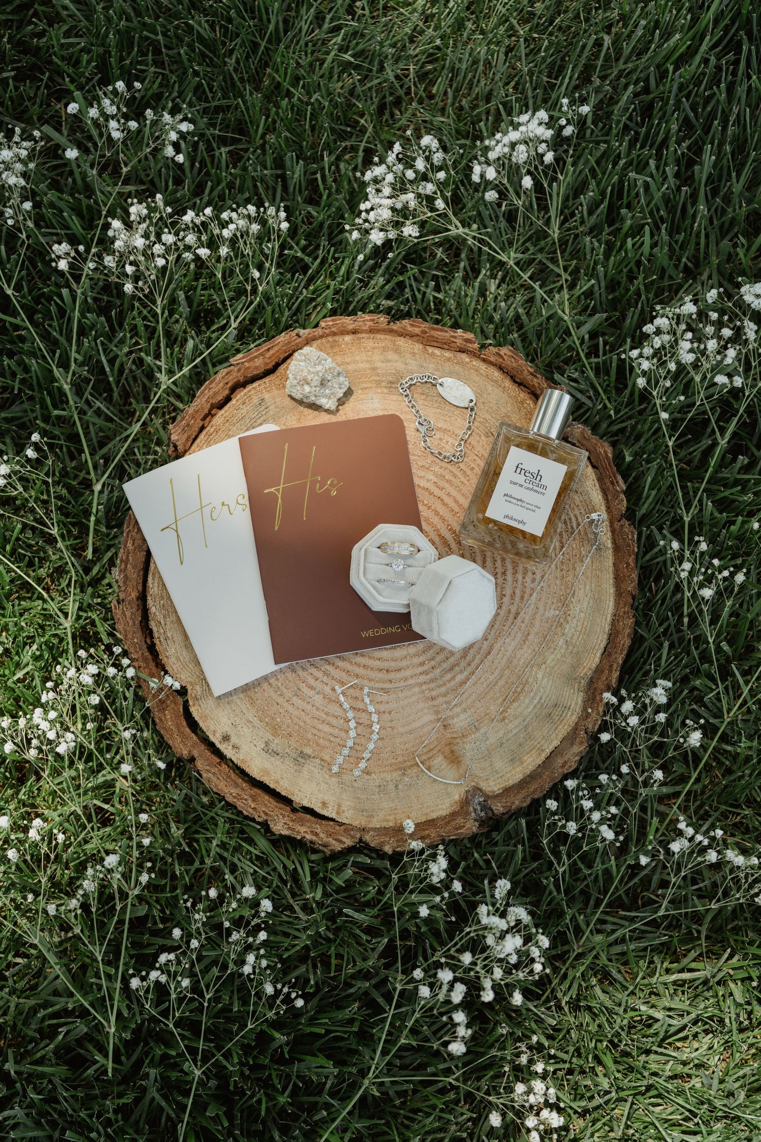 Flat lay of wedding vows books and decorative items on wooden slice with white flowers.
