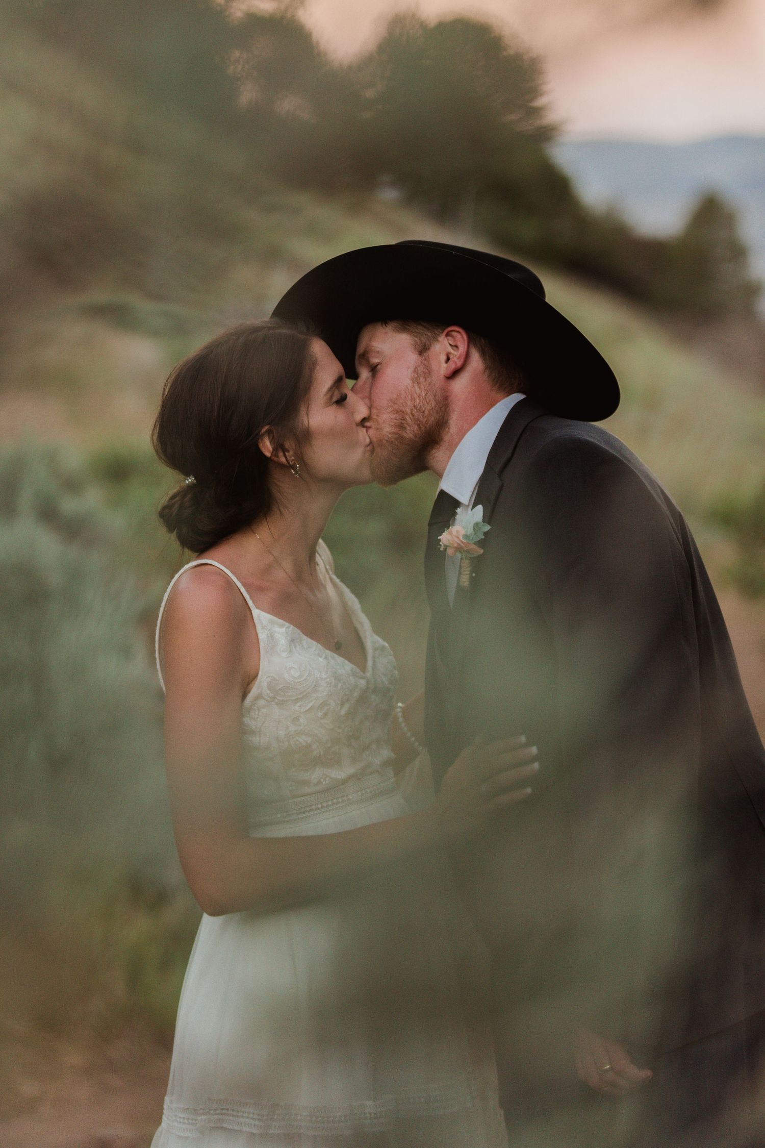 A romantic kiss between newlyweds in a field at sunset with dreamy bokeh effect.