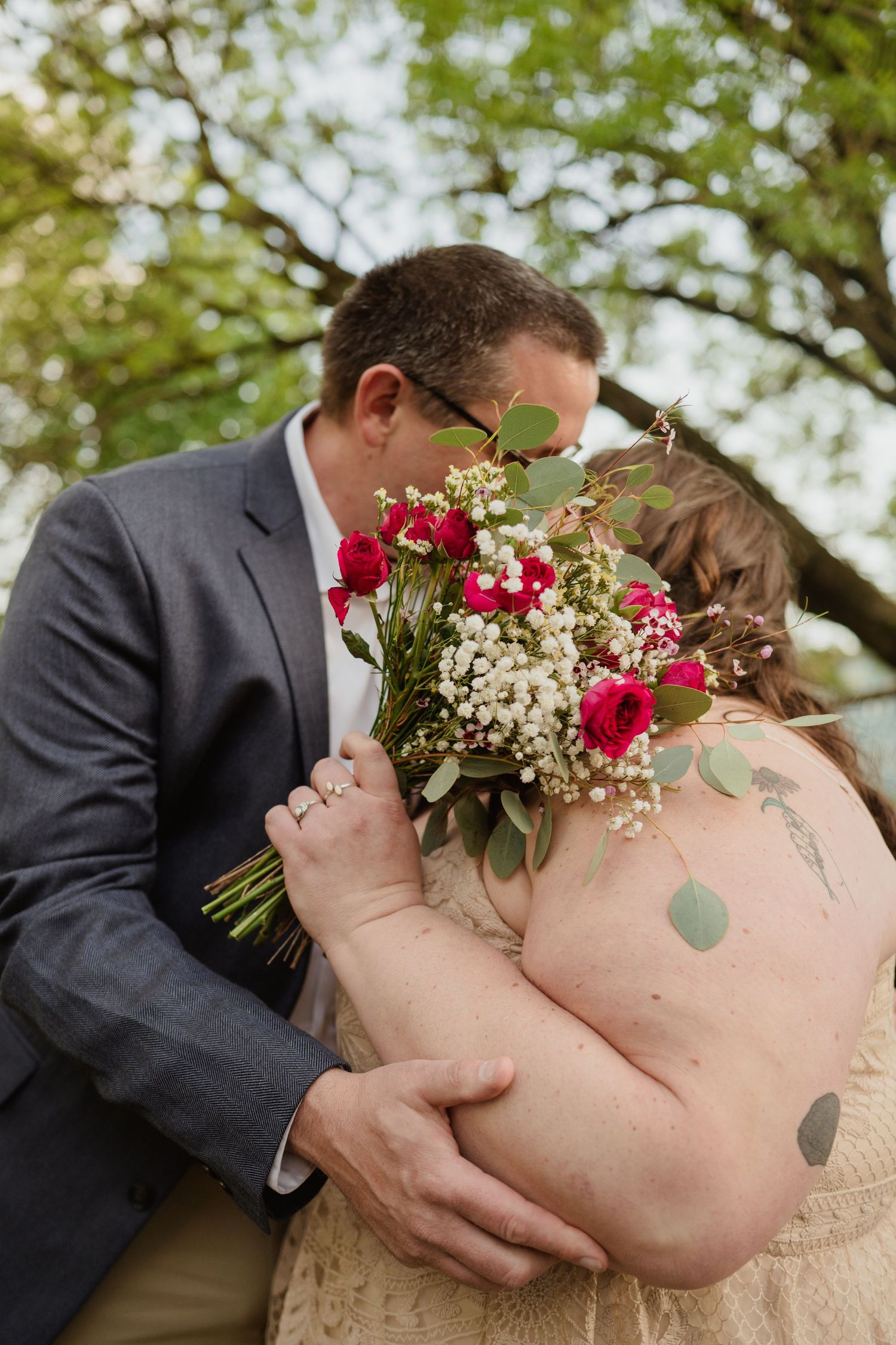 A couple shares an intimate moment with a bouquet of red and white flowers during their wedding photos.