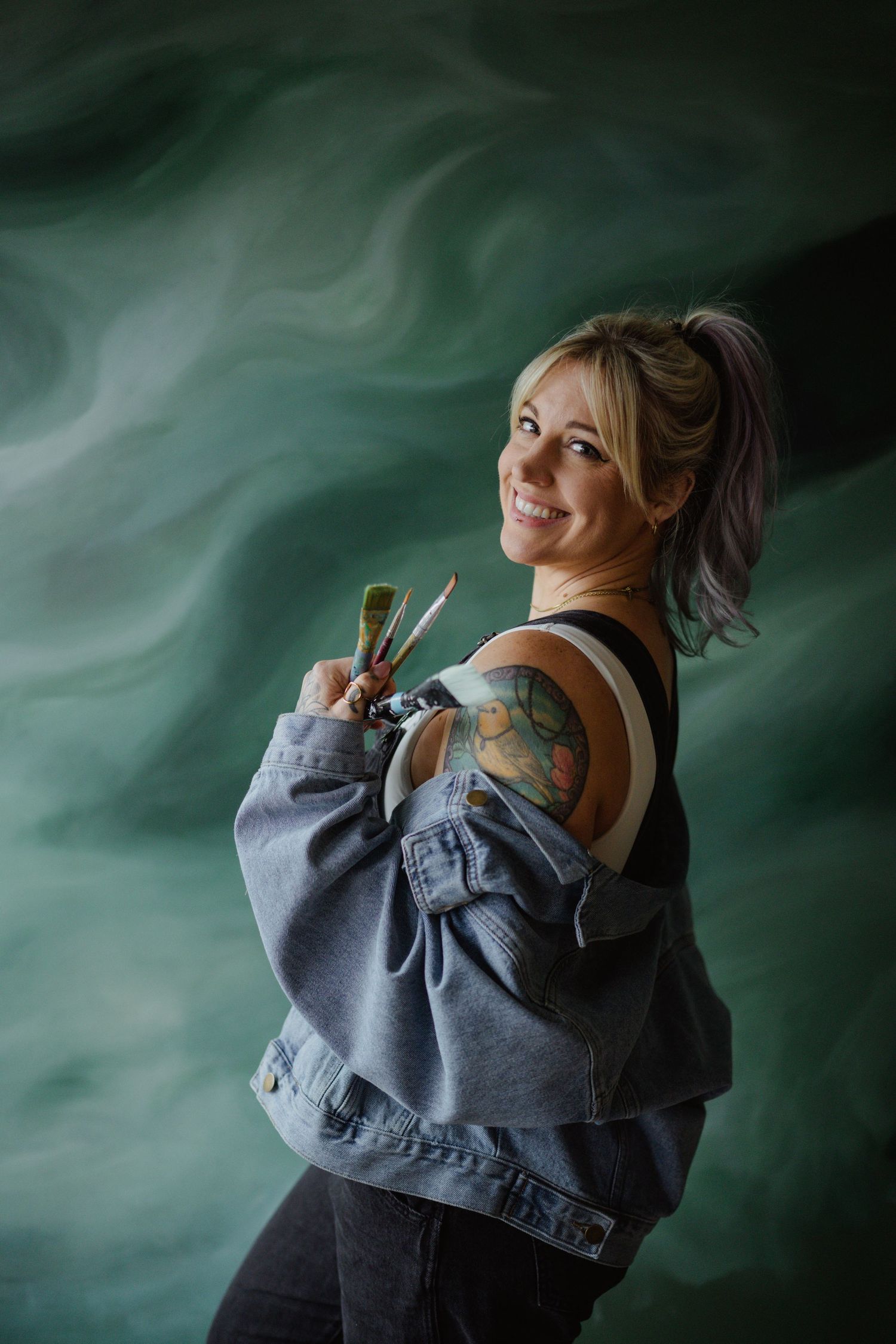 An artist holds painting brushes against a dramatic green backdrop.