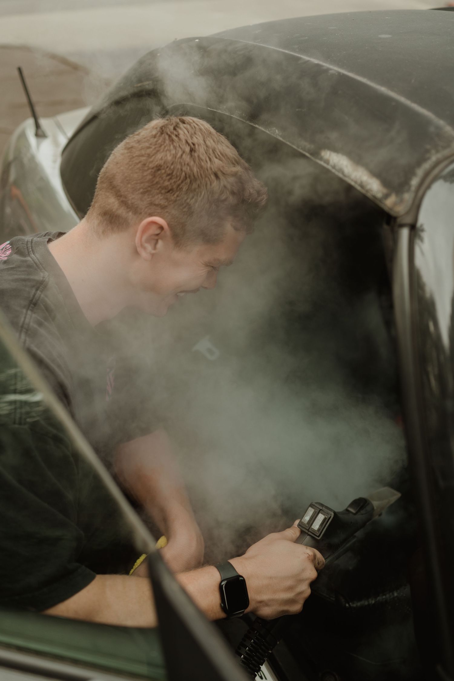 Person detailing car interior surrounded by steam or cleaning vapor.