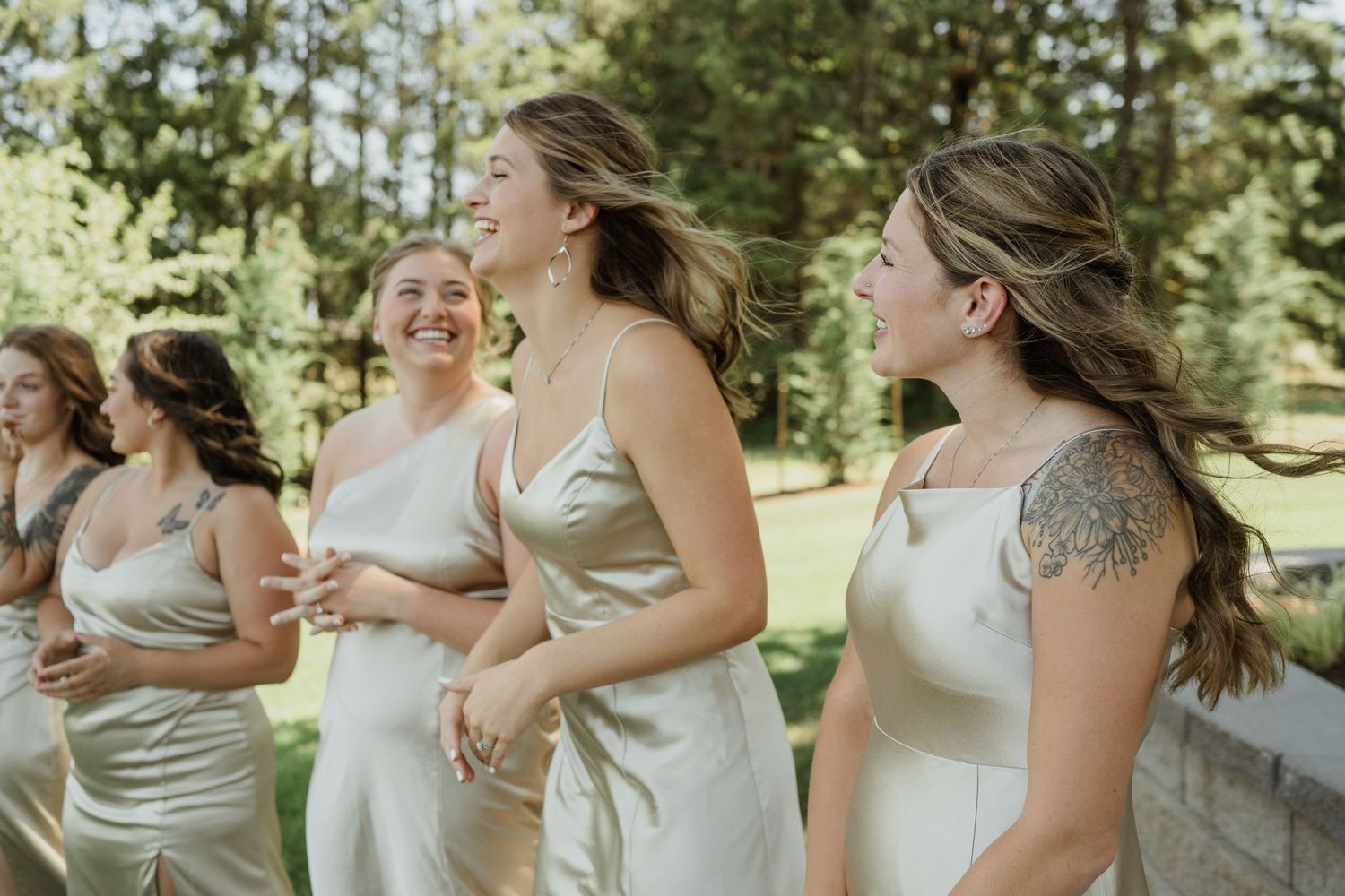 Bridesmaids in champagne-colored dresses share a joyful moment outdoors.