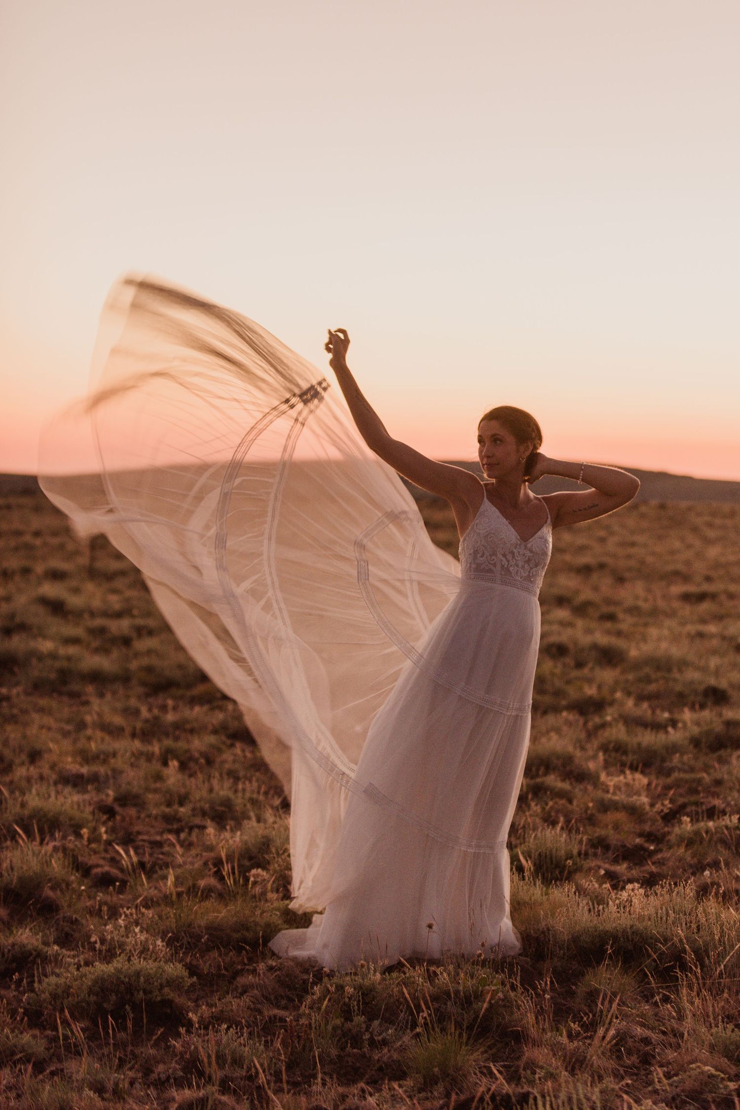 A flowing white wedding dress catches the wind during sunset in an open field.