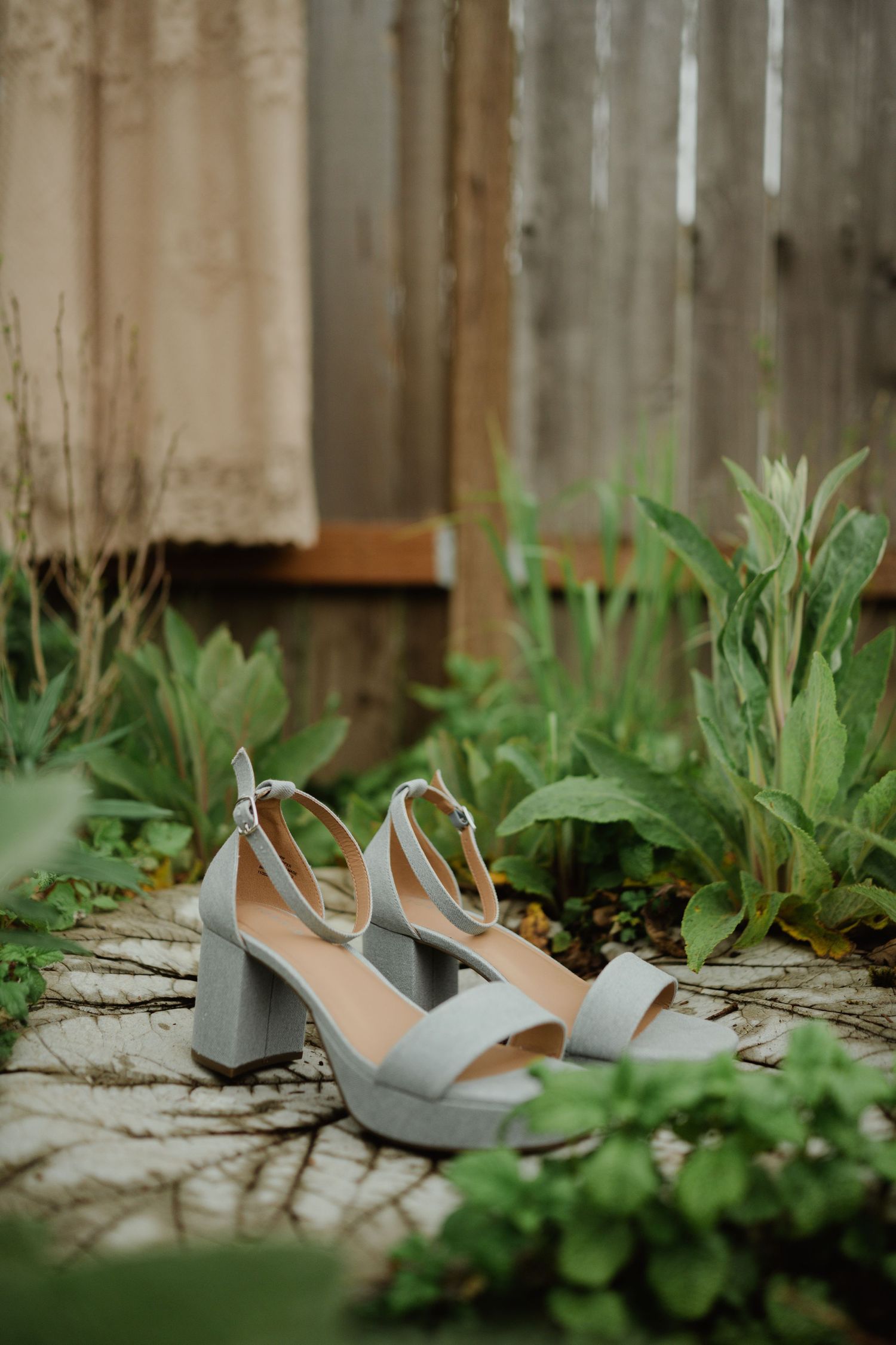 Light gray wedding heels placed among garden foliage and stepping stones.