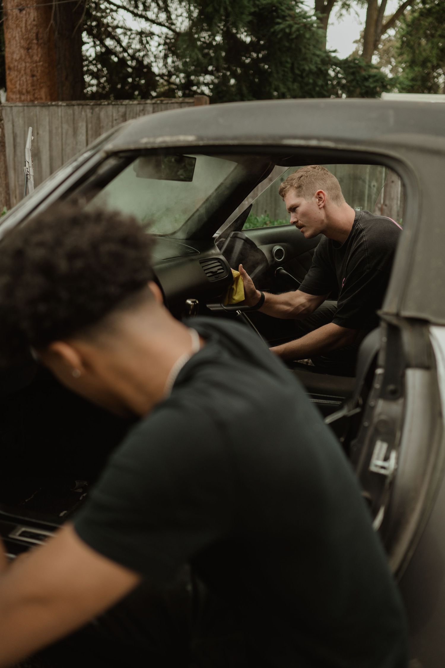 Two people working on detailing the interior of a classic car.