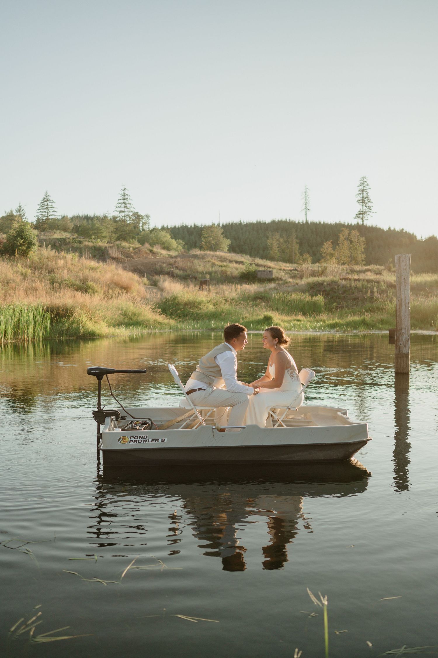 A romantic boat scene with a couple in wedding attire on calm waters at sunset.