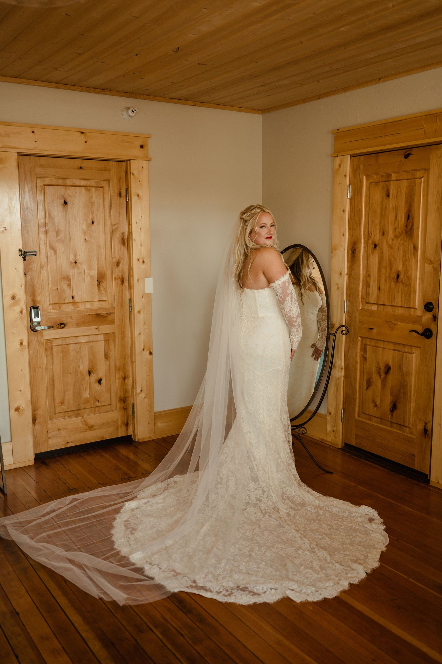 A bride in a lace wedding gown with long train poses in a rustic wooden room.
