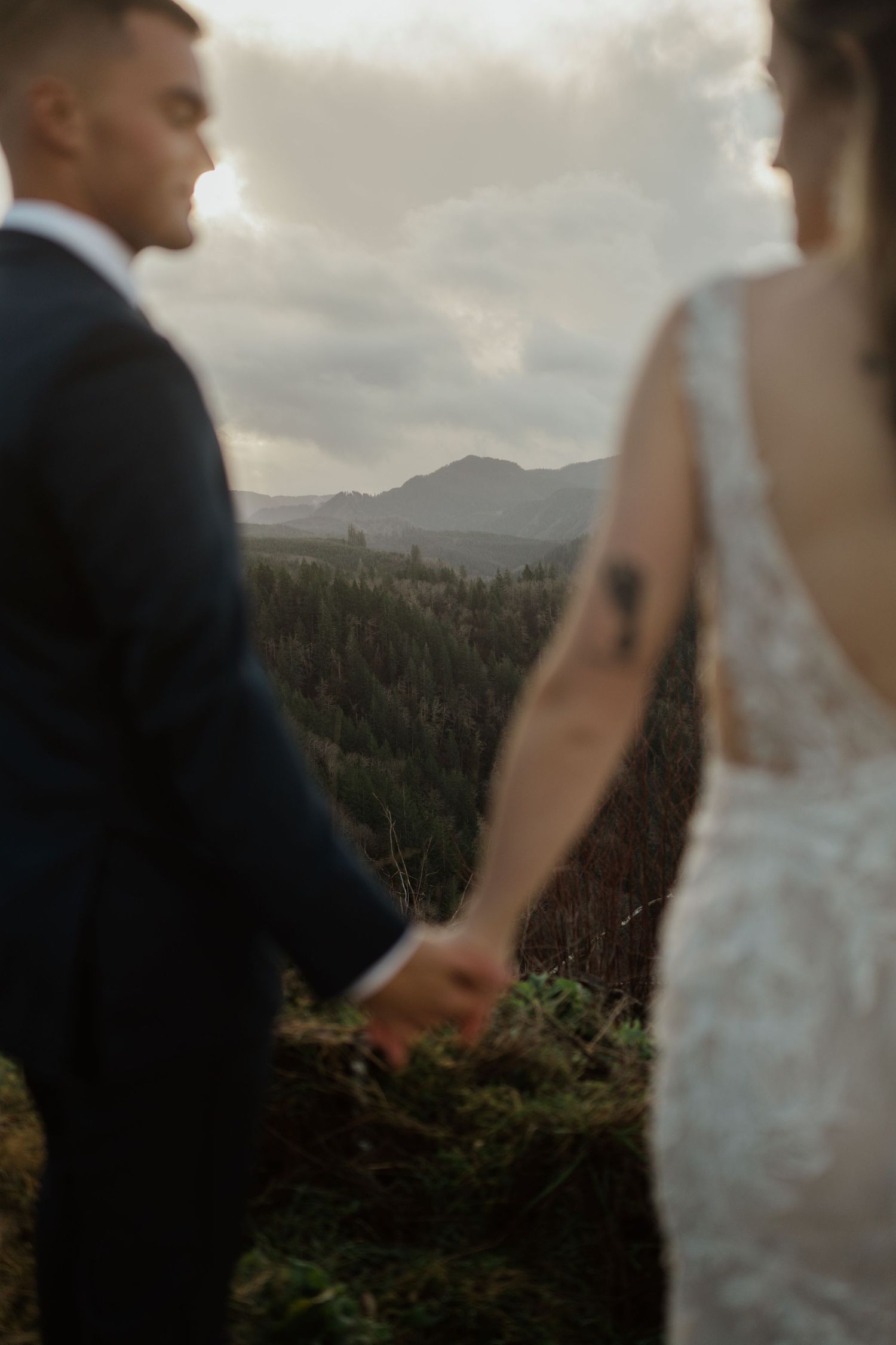 A couple holds hands while overlooking a mountain landscape at sunset.