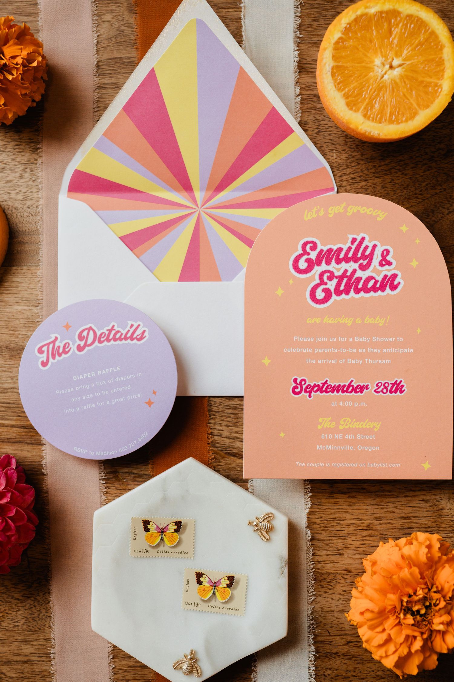 Colorful wedding invitation suite with geometric envelope liner, orange slices, and floral accents on wooden surface.