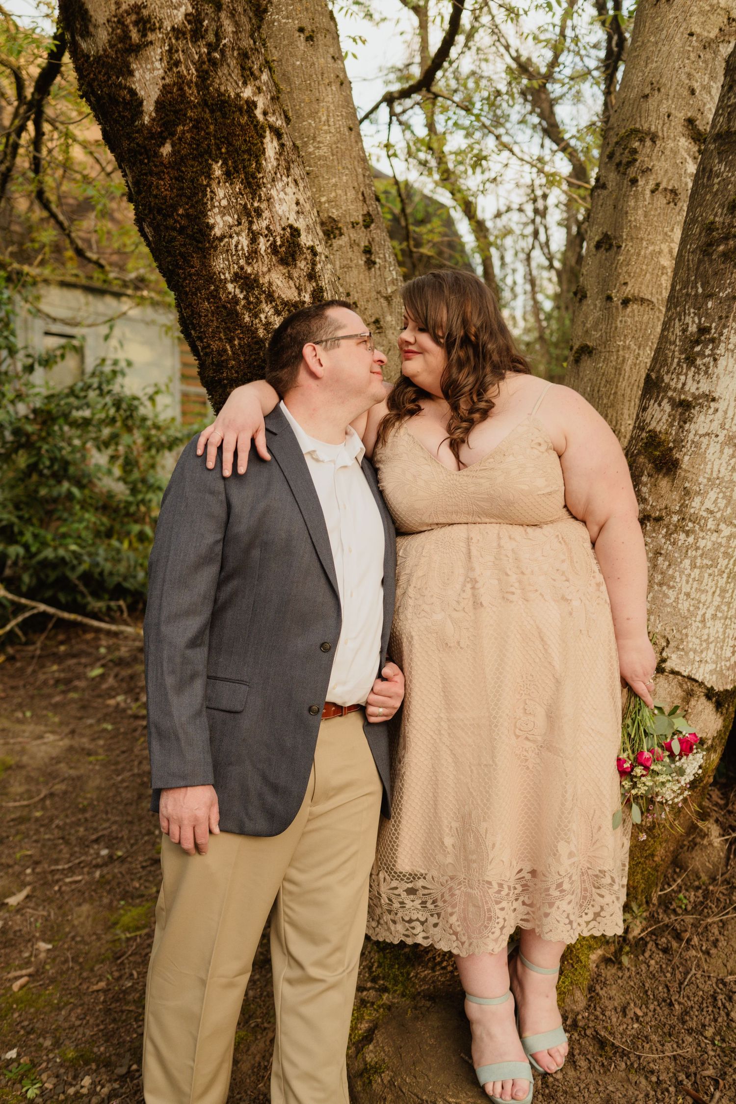 A couple shares a tender moment leaning against a tree trunk during their wedding photoshoot.