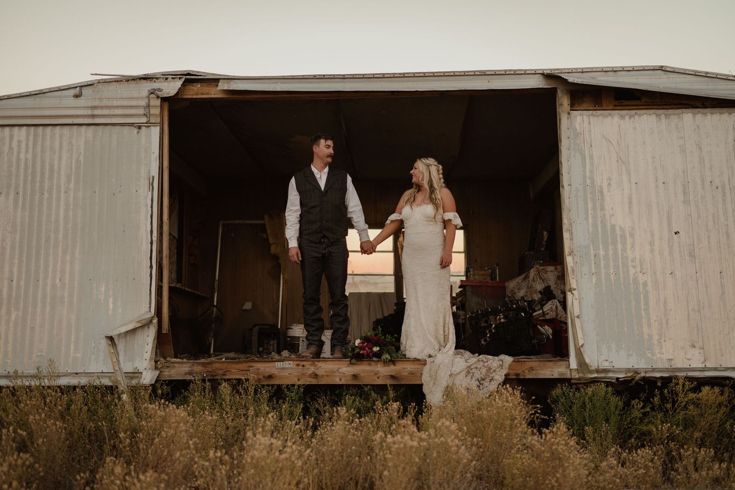 A rustic wedding photo shoot at an old barn with a couple standing in the doorway at sunset.
