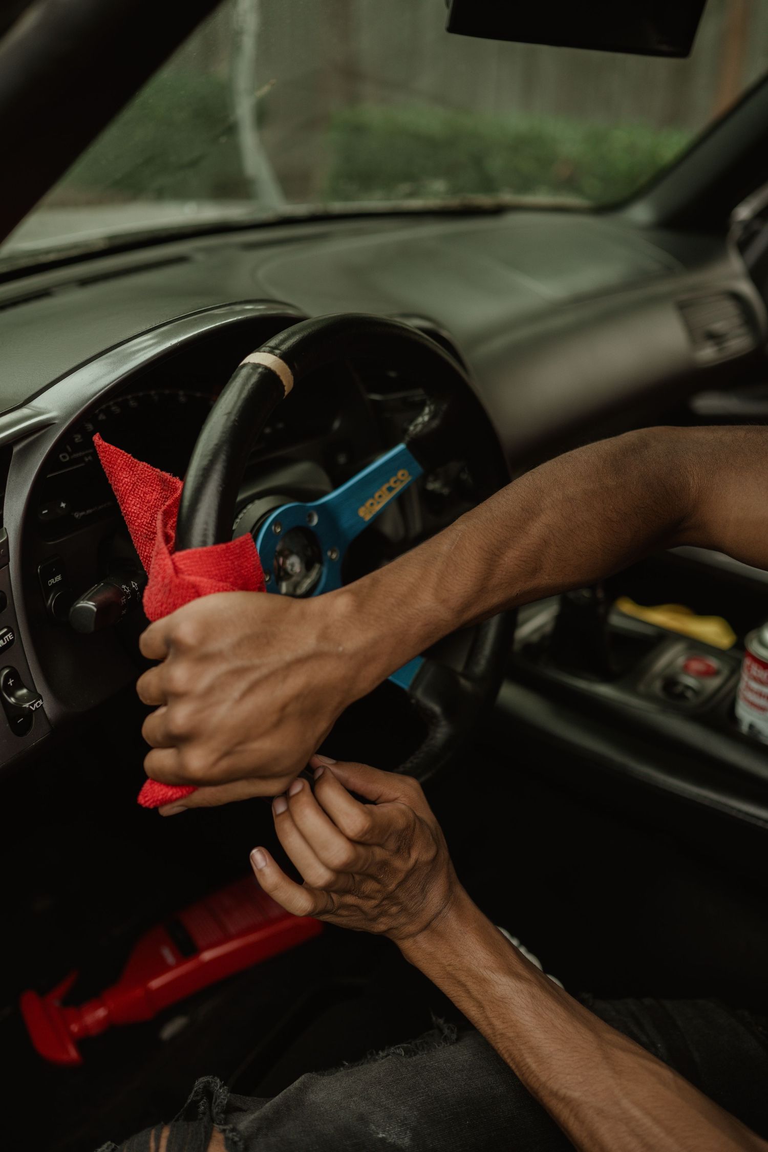 Hands cleaning car dashboard with red cloth and blue tool.