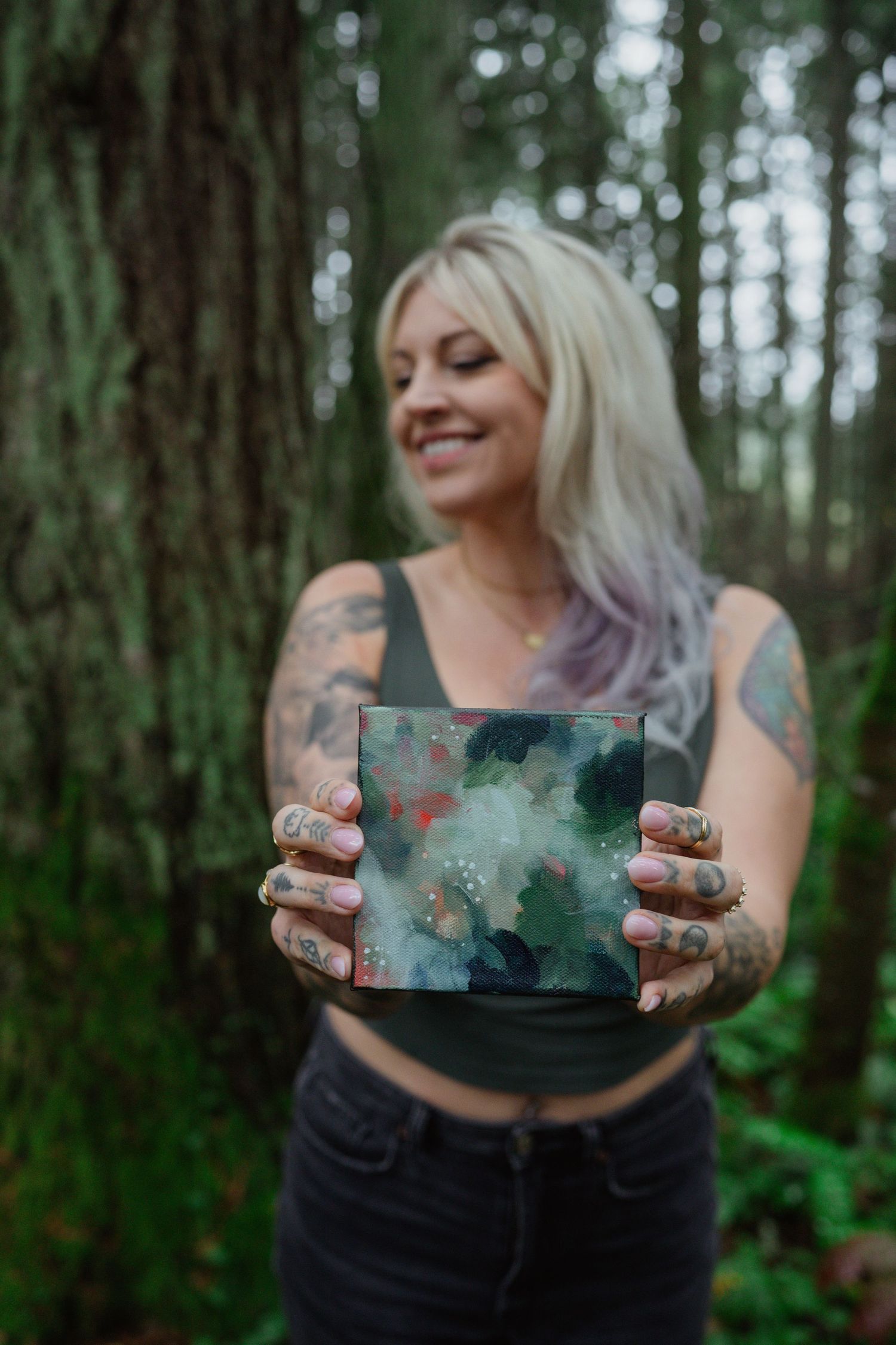 Artist displaying small artwork outdoors in a lush forest setting.