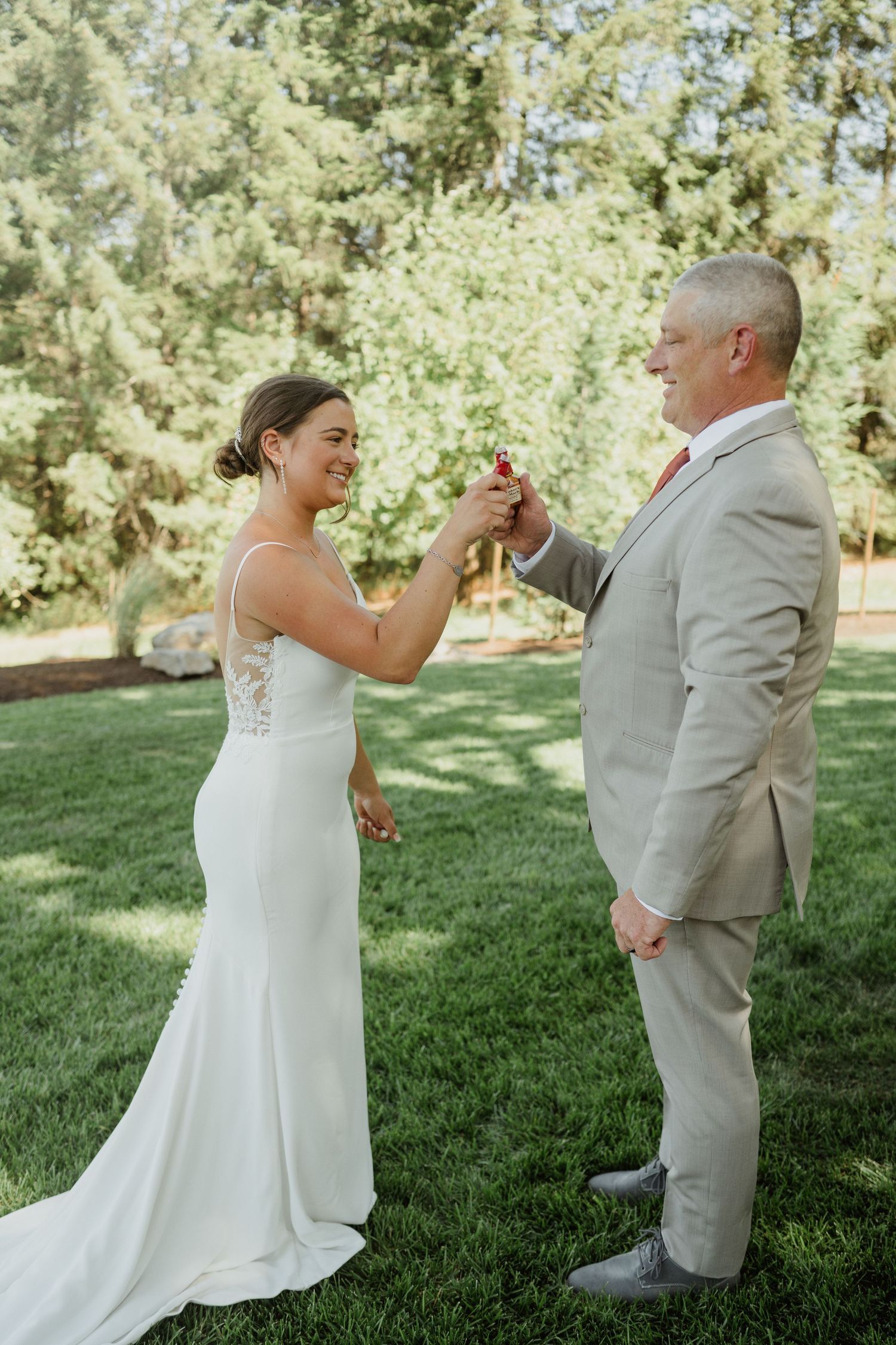 A couple in wedding attire holding hands and sharing a joyful moment on a lawn.