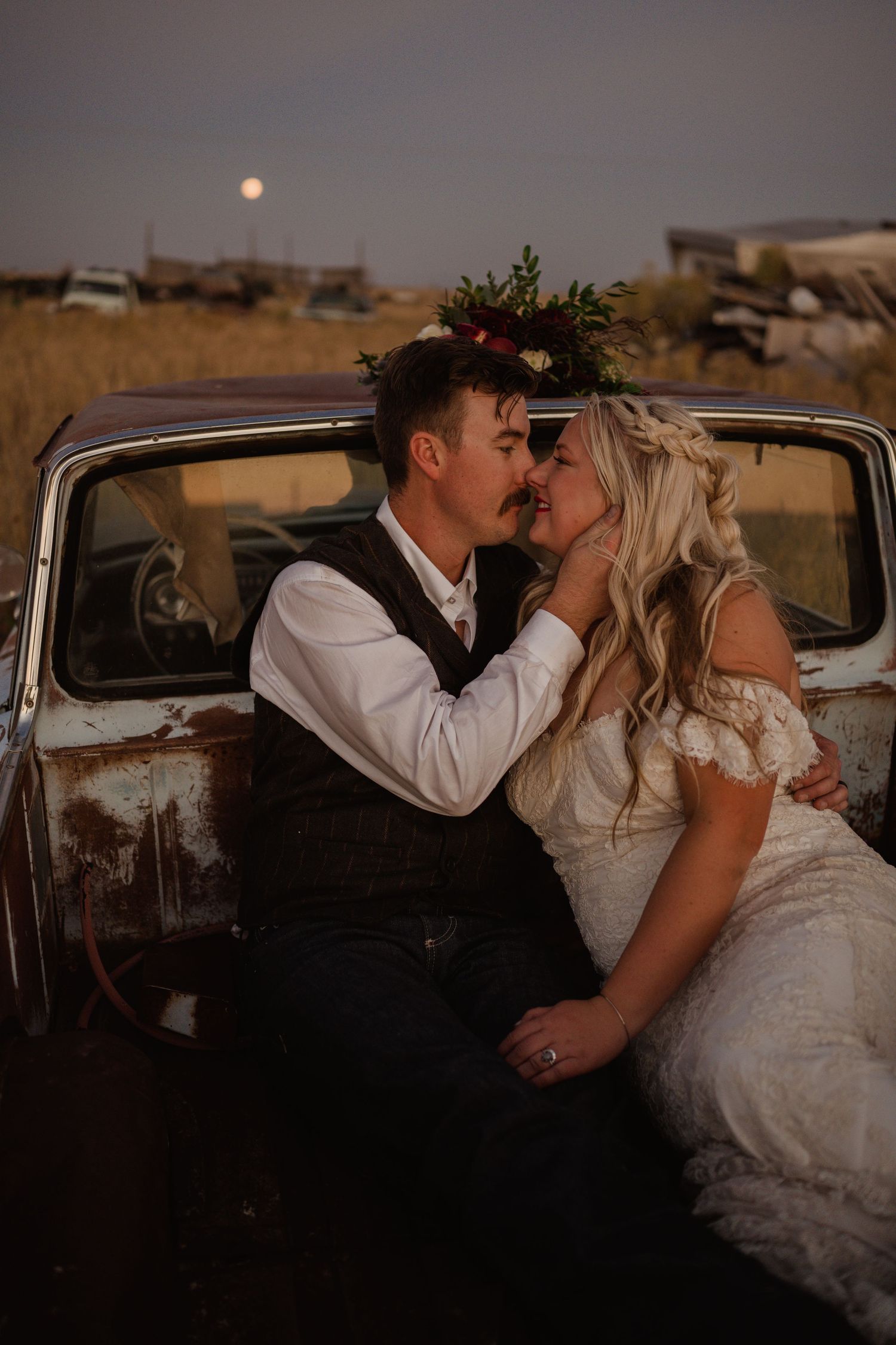 Romantic wedding portrait in an antique car with the moon visible in the background.