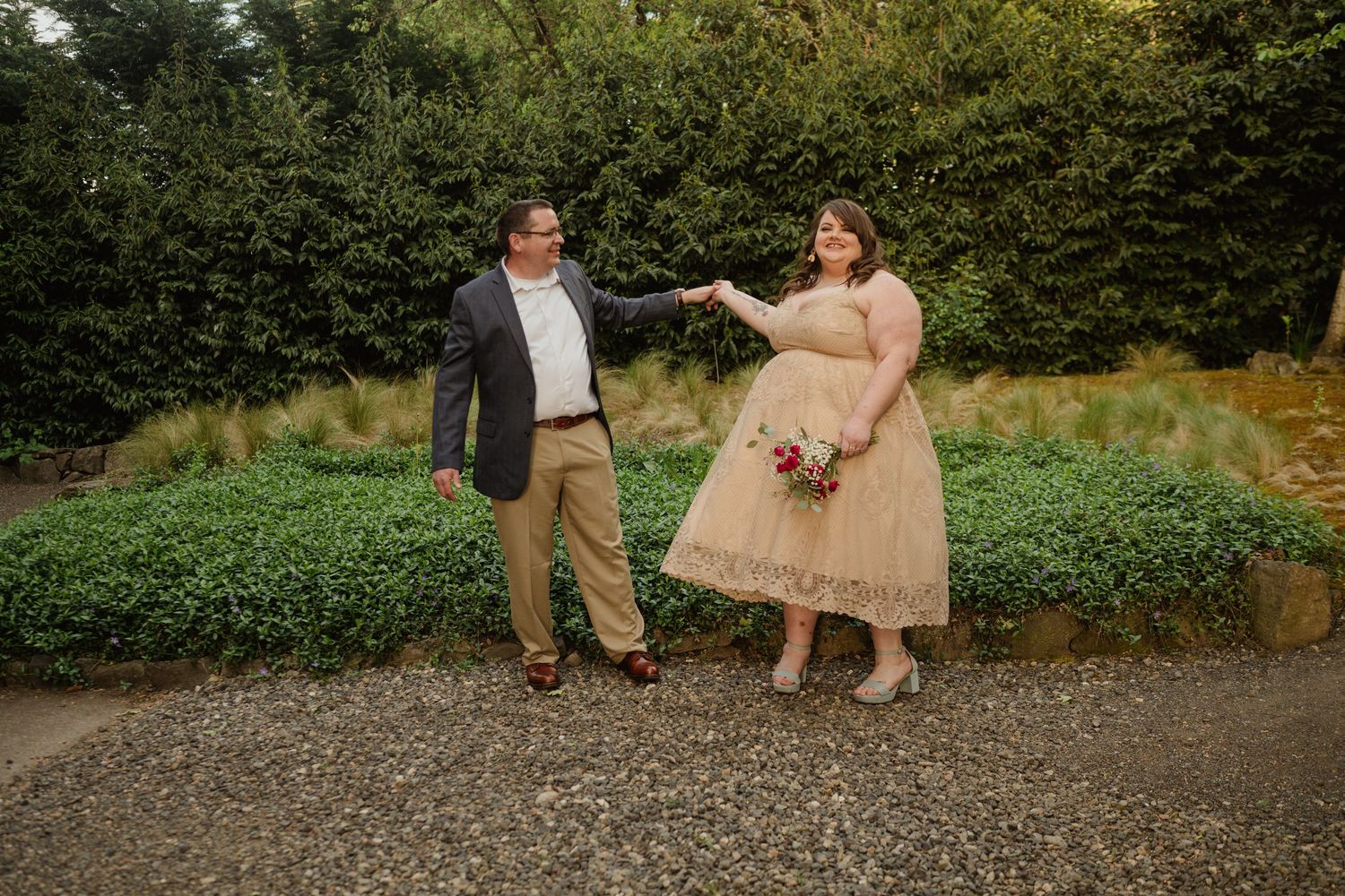 A couple in wedding attire dances playfully in a garden setting.