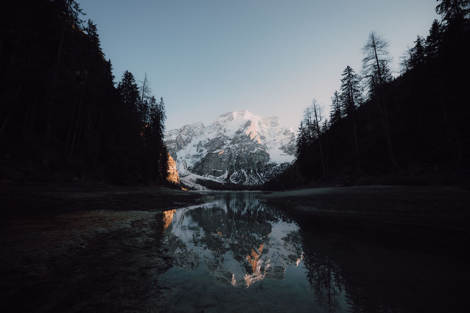 Mountain landscape mirrored in calm lake water with evergreen trees framing the scene.