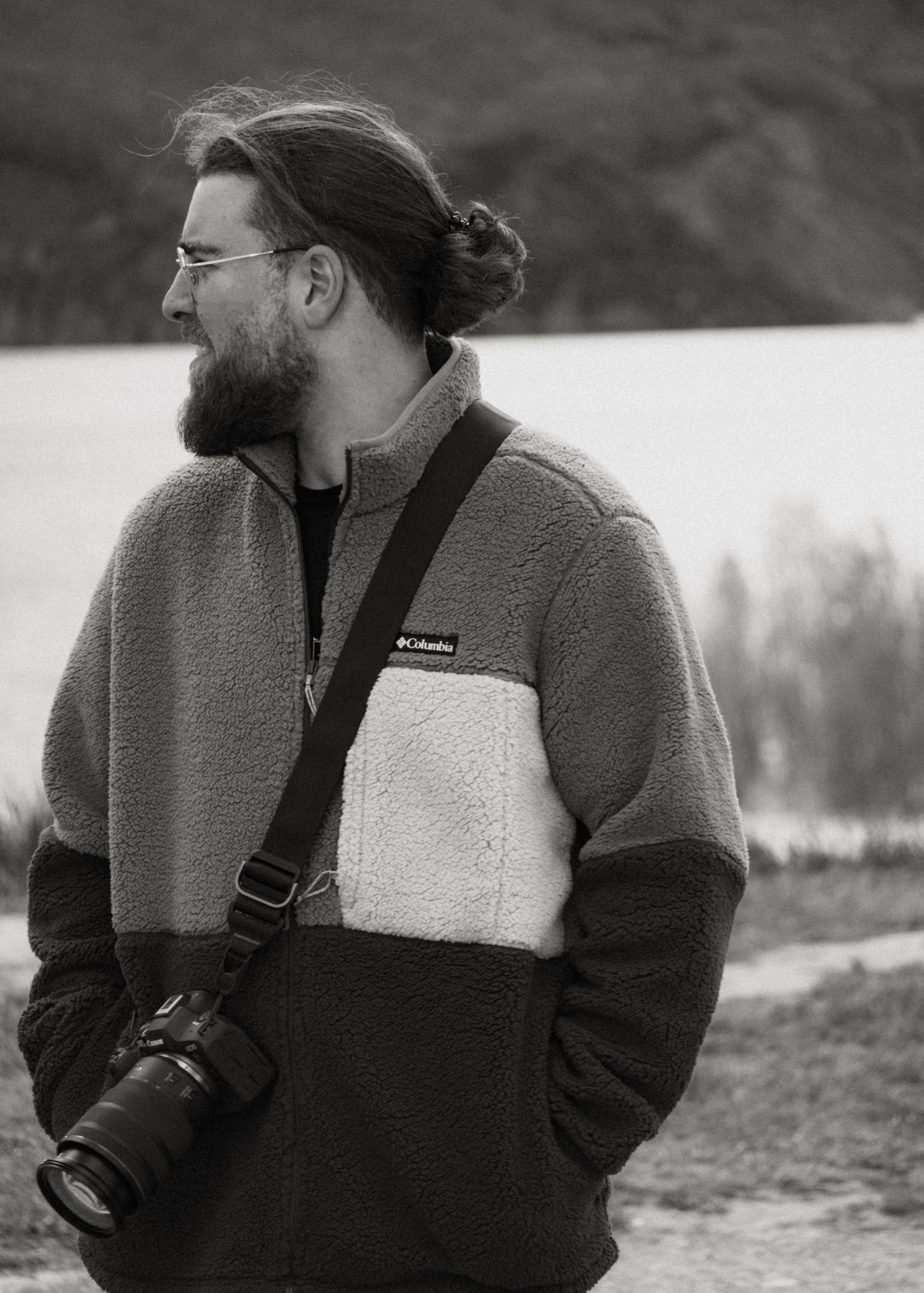 A photographer in a fleece jacket gazes into the distance while holding camera equipment.