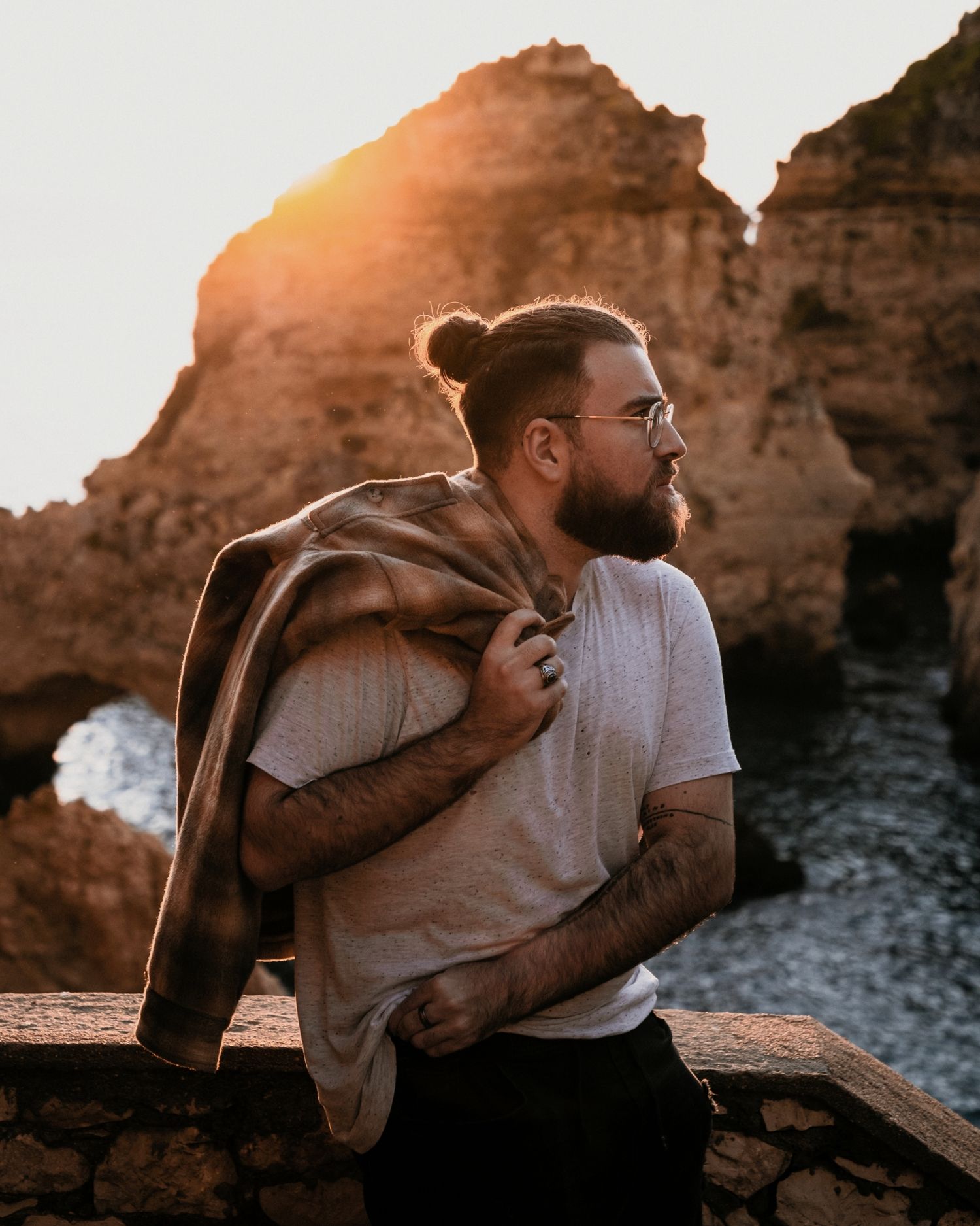 A photographer stands against a rocky coastal backdrop at golden hour.
