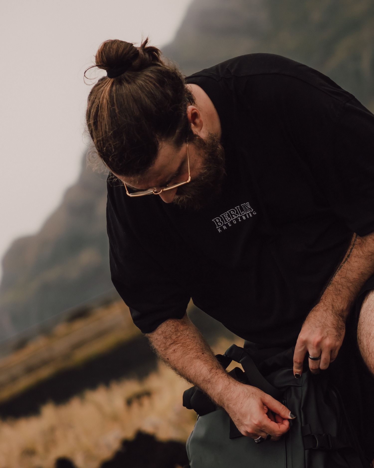 Person in black sweatshirt looking down while outdoors in mountainous setting.