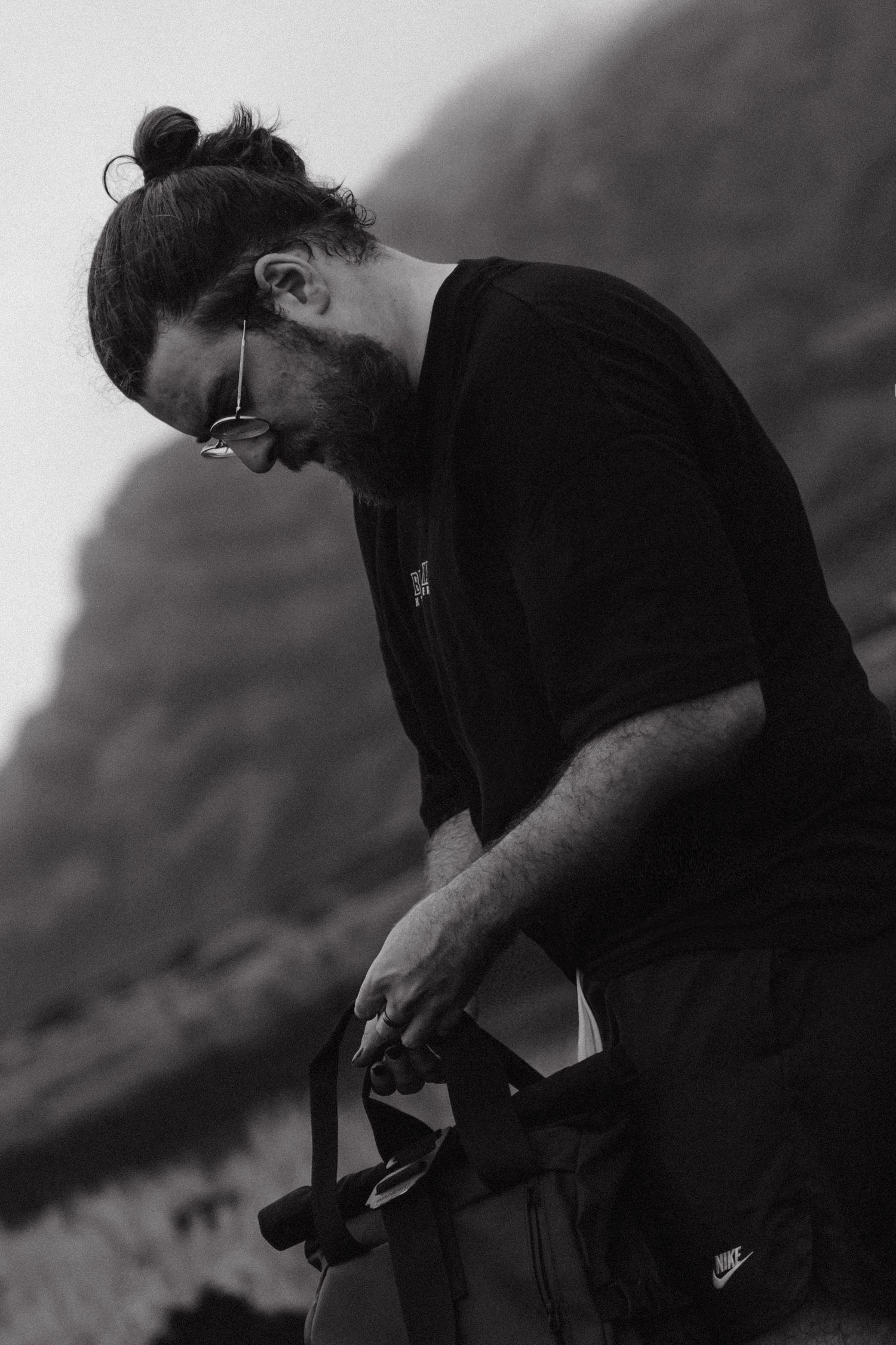 A photographer adjusts camera settings while standing against a mountainous background.