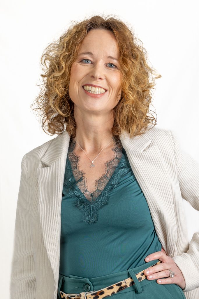Professional portrait of someone with curly blonde hair wearing a white blazer and teal camisole with lace trim against white background.