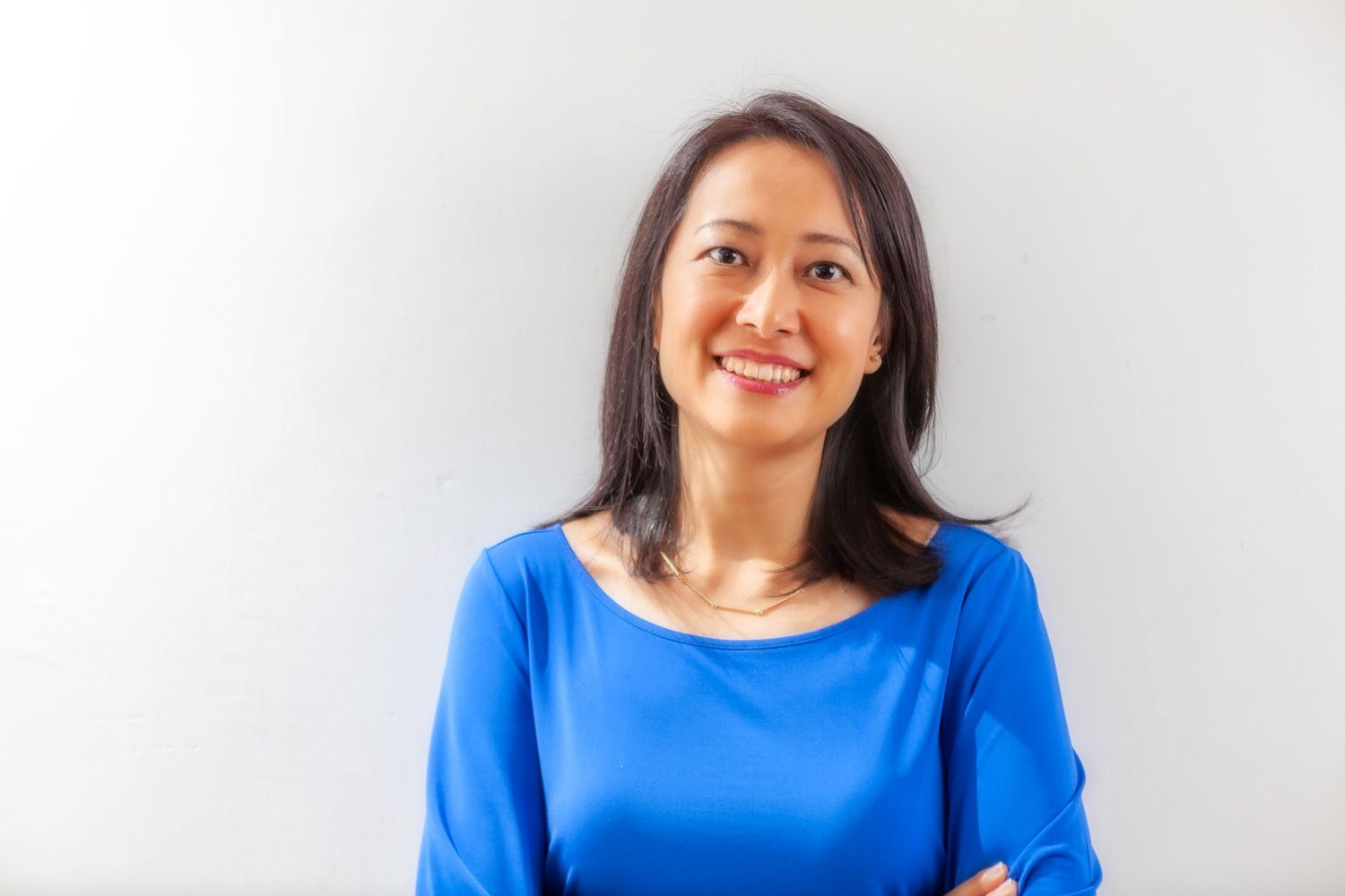 Professional portrait of someone in a bright blue sweater smiling warmly against a light gray background.