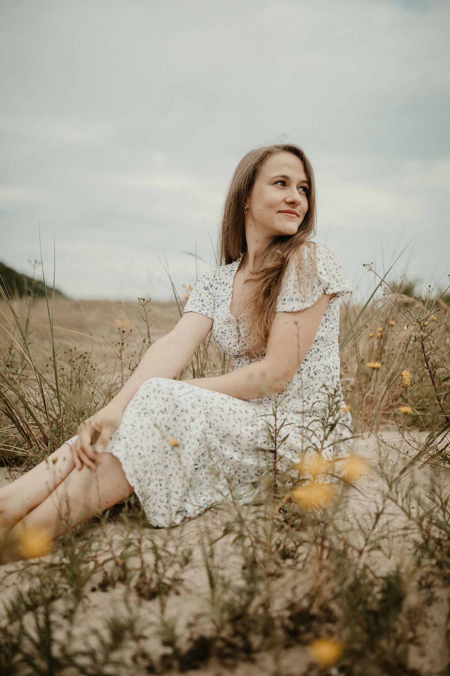 Frau in Blumenkleid sitzt während der goldenen Stunde auf einem Feld mit Wildblumen.