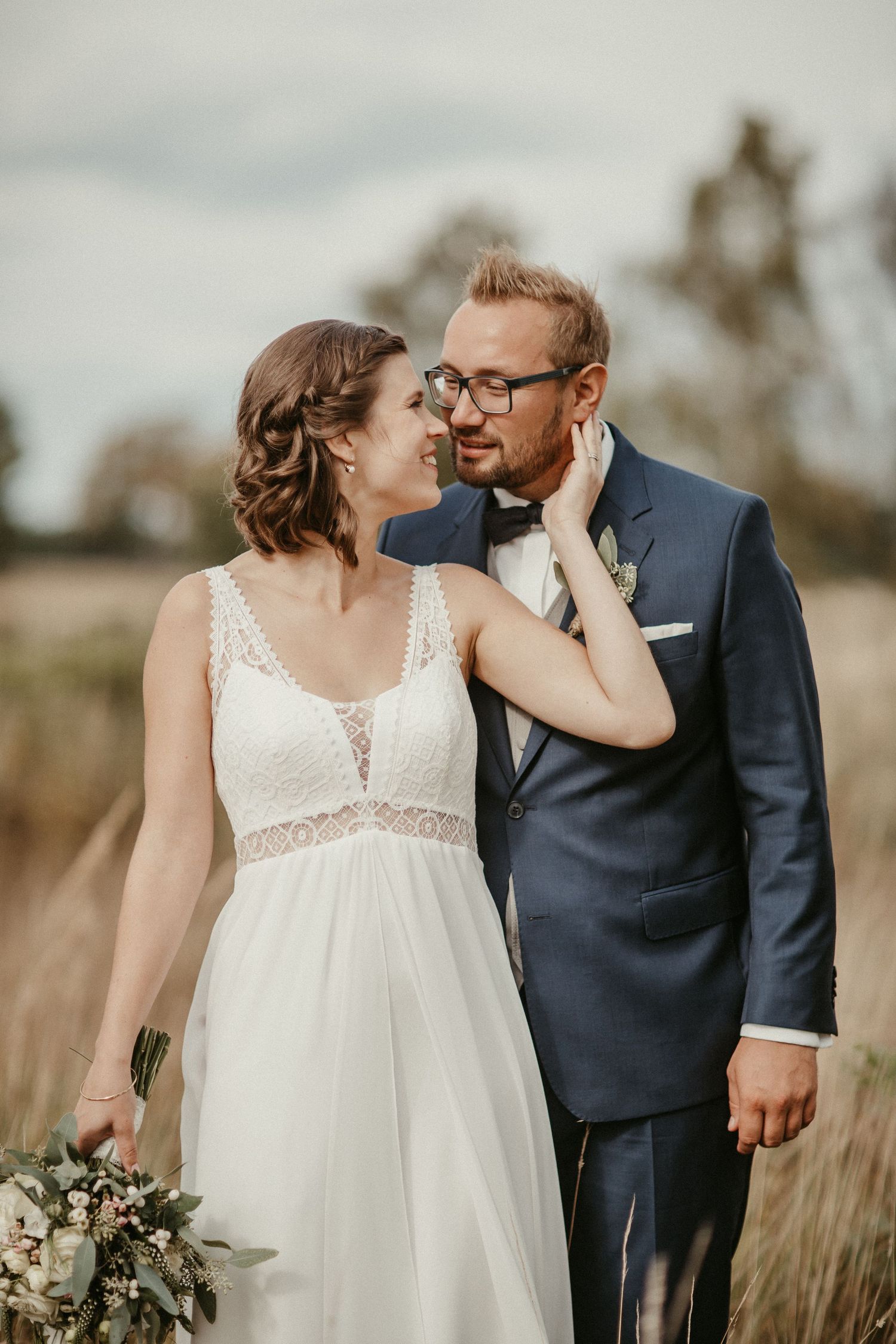 Romantisches Hochzeitsporträt eines Paares auf einem Feld mit der Braut in einem fließenden Spitzenkleid.