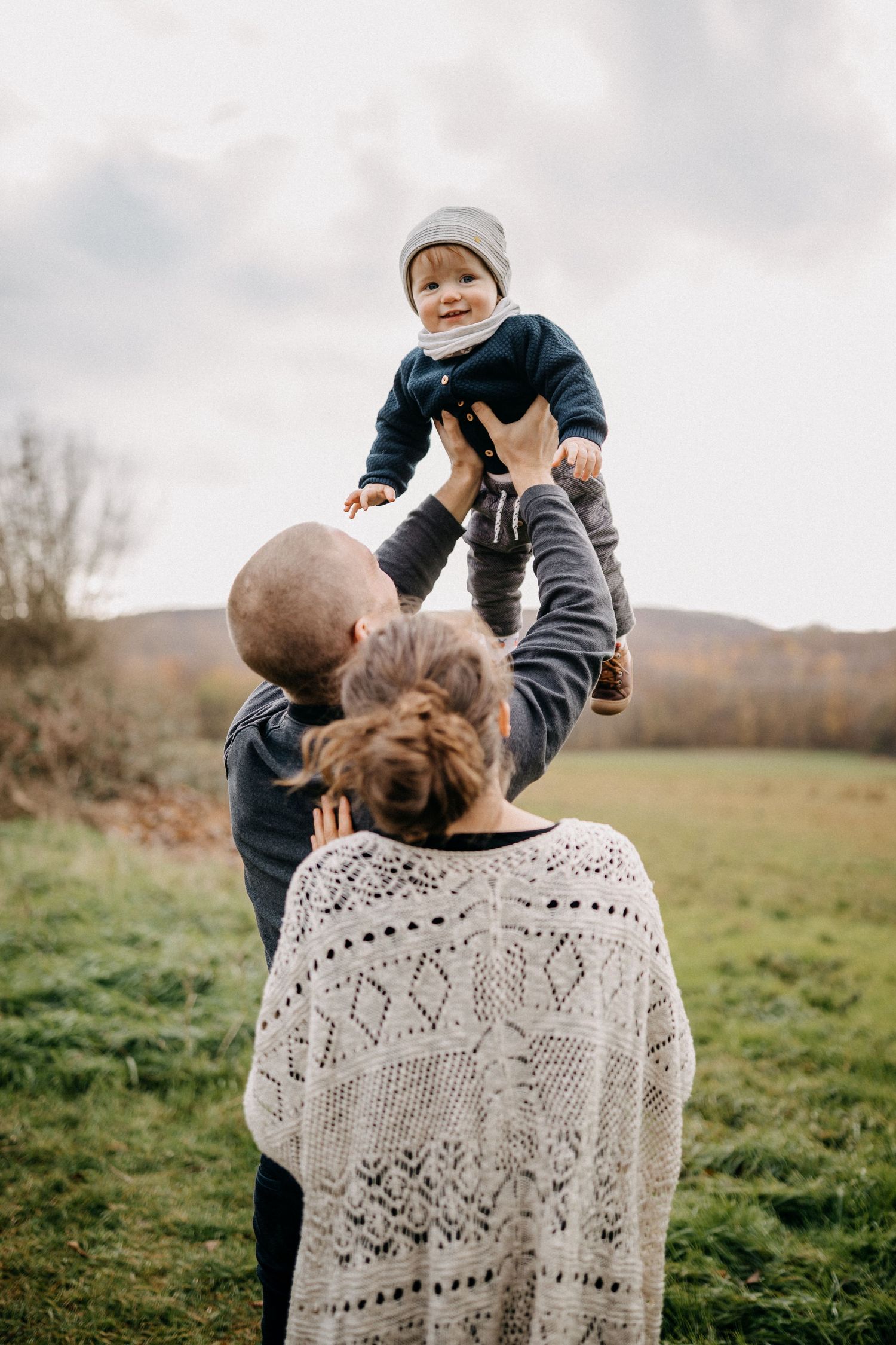 Ein freudiger Familienmoment, der auf einer Wiese festgehalten wird, während ein Kind in die Luft gehoben wird.