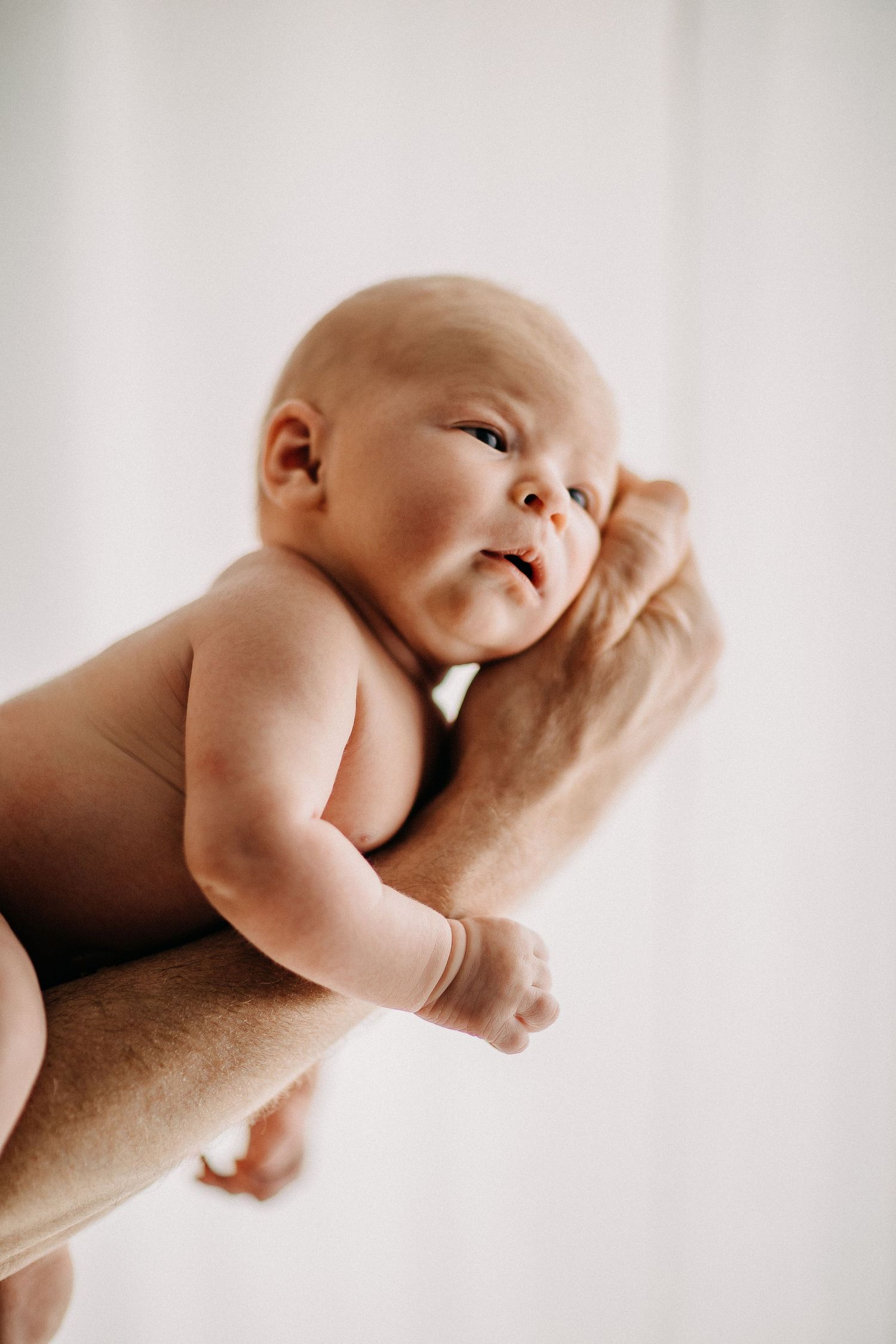 Ein neugeborenes Baby ruht sanft auf unterstützenden Händen in einer minimalistischen Hochformatumgebung.