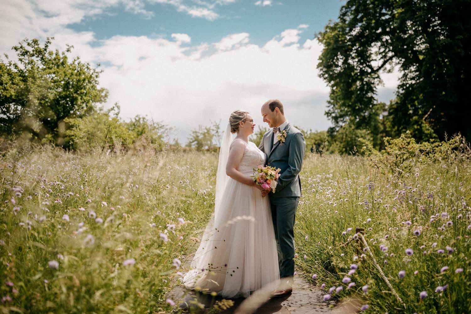 Hochzeitspaar steht zusammen auf einer Wildblumenwiese an einem sonnigen Sommertag.