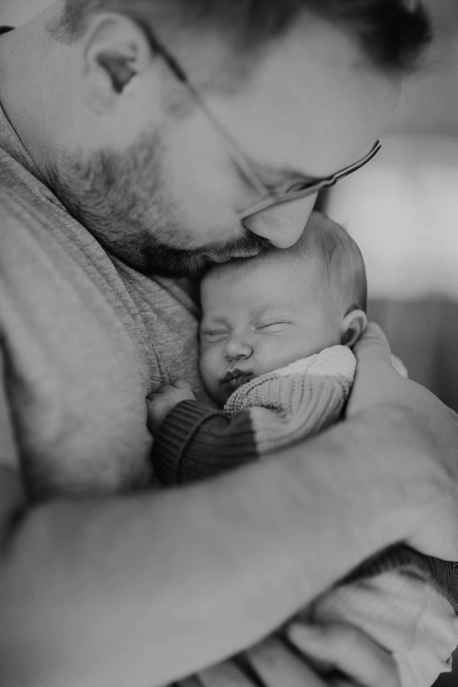 Intimes Schwarz-Weiß-Porträt eines Babys, das gegen die Brust eines Erwachsenen schläft.