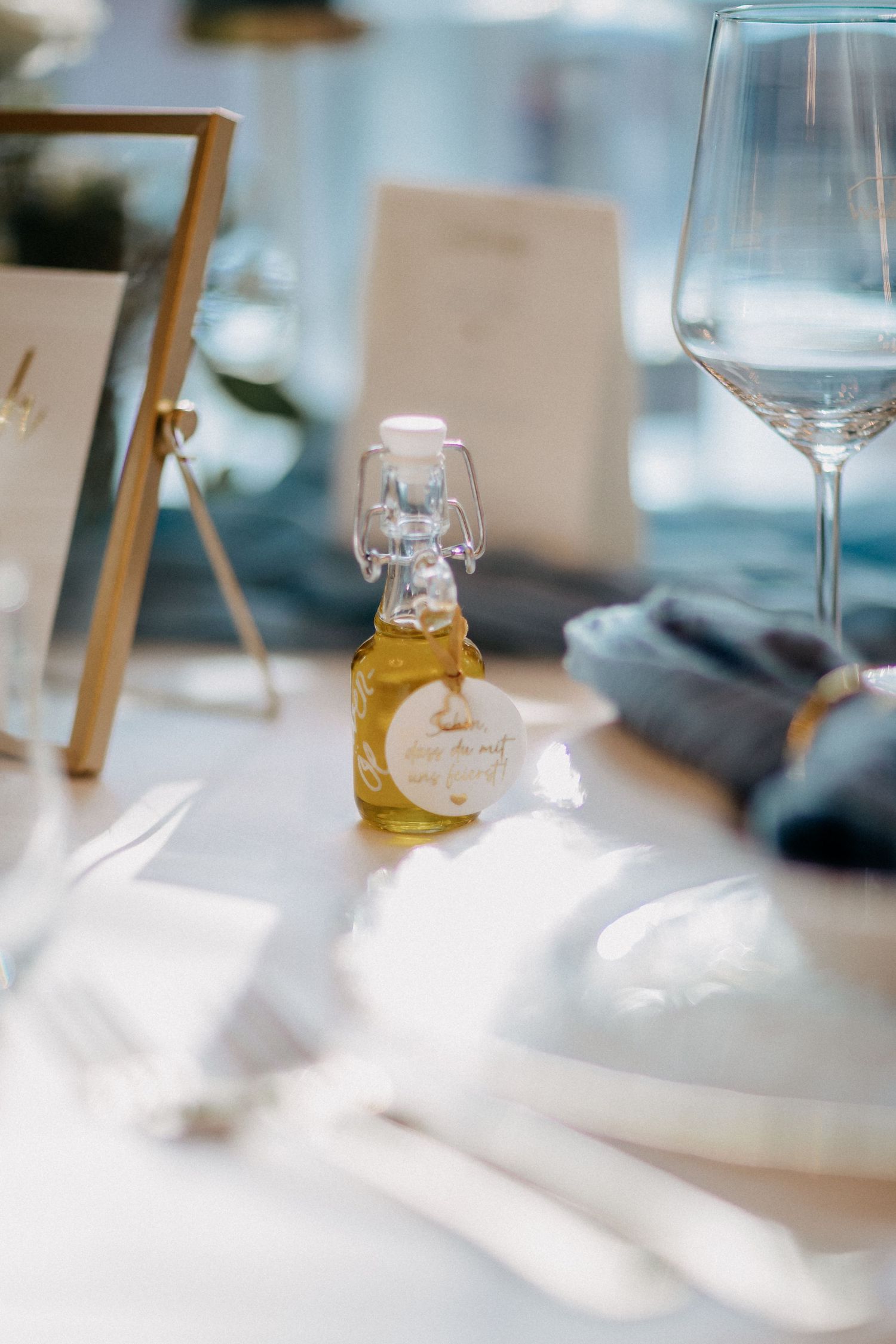 Eine elegante Hochzeitsdekoration mit Weingläsern und einer kleinen dekorativen Flasche auf einer weißen Tischdecke im Waldhaus Ölper.