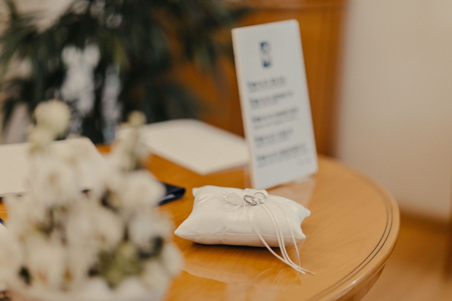 Eheringkissen und Briefpapier auf Holztisch mit weißen Blumendekorationen.