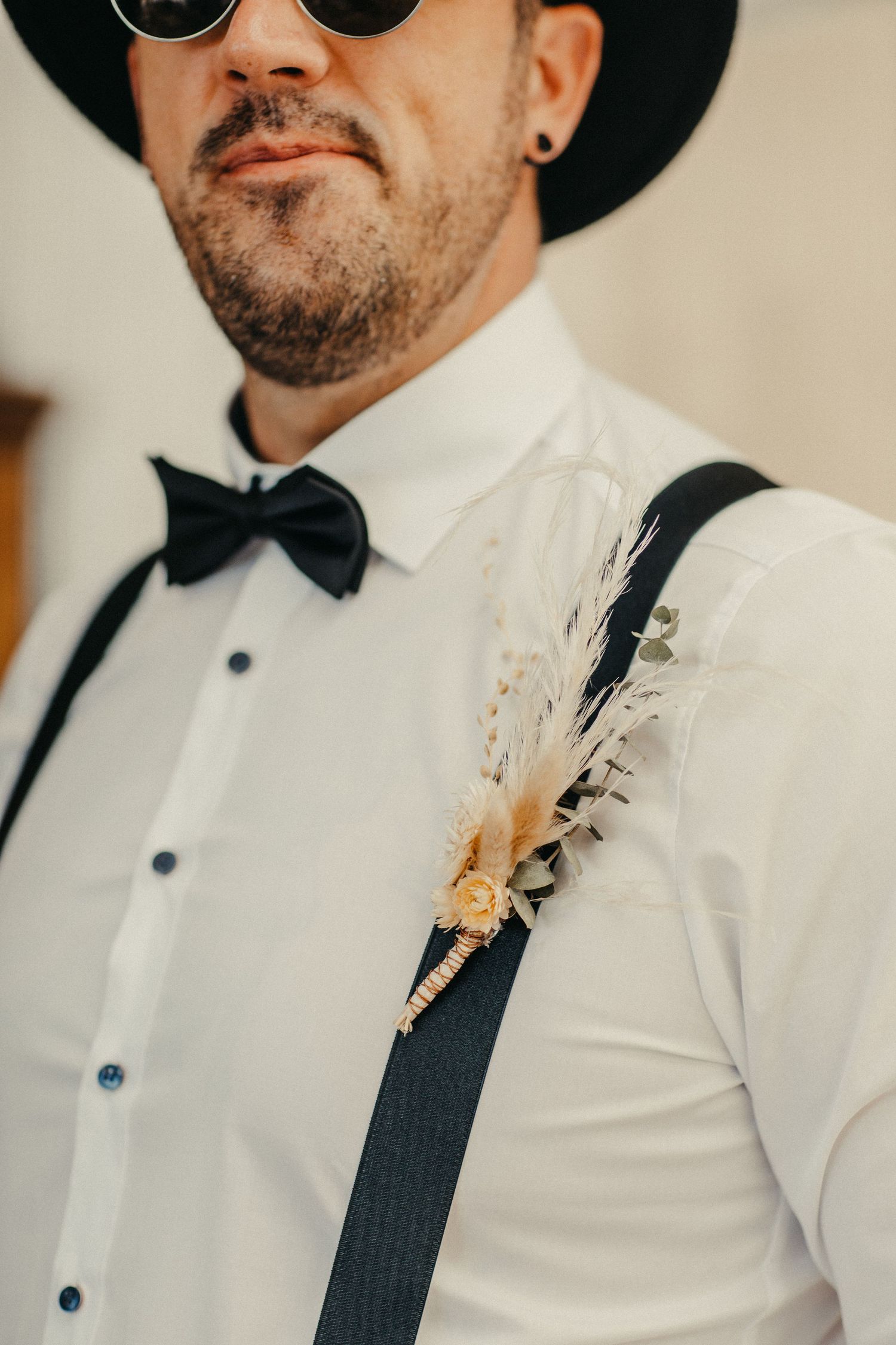 Stilvoller Bräutigam in weißem Hemd, Fliege und Hosenträgern mit Sonnenbrille und Fedora.