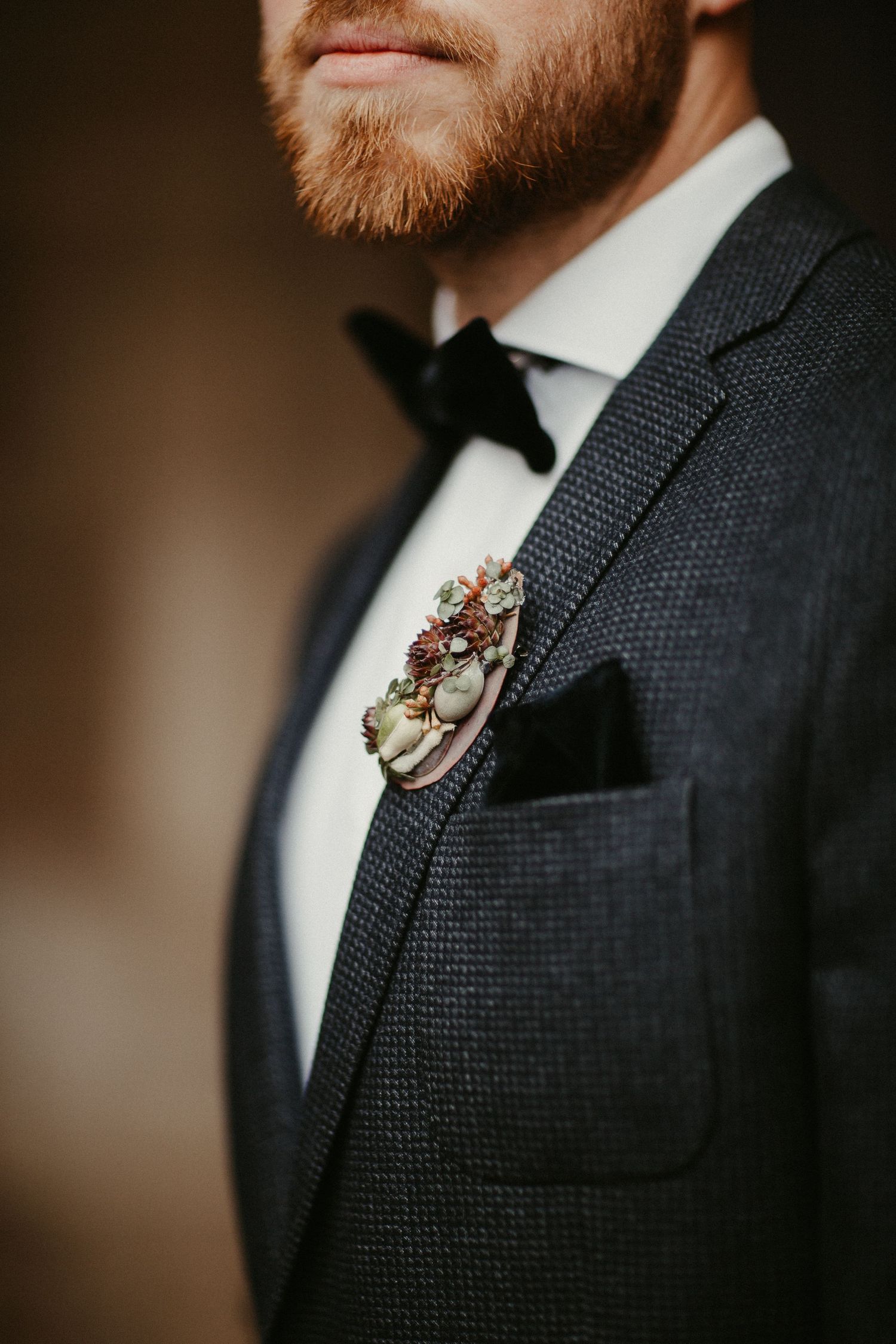 Nahaufnahme des schwarzen Smokings des Bräutigams mit geblümter Boutonniere und Fliege.