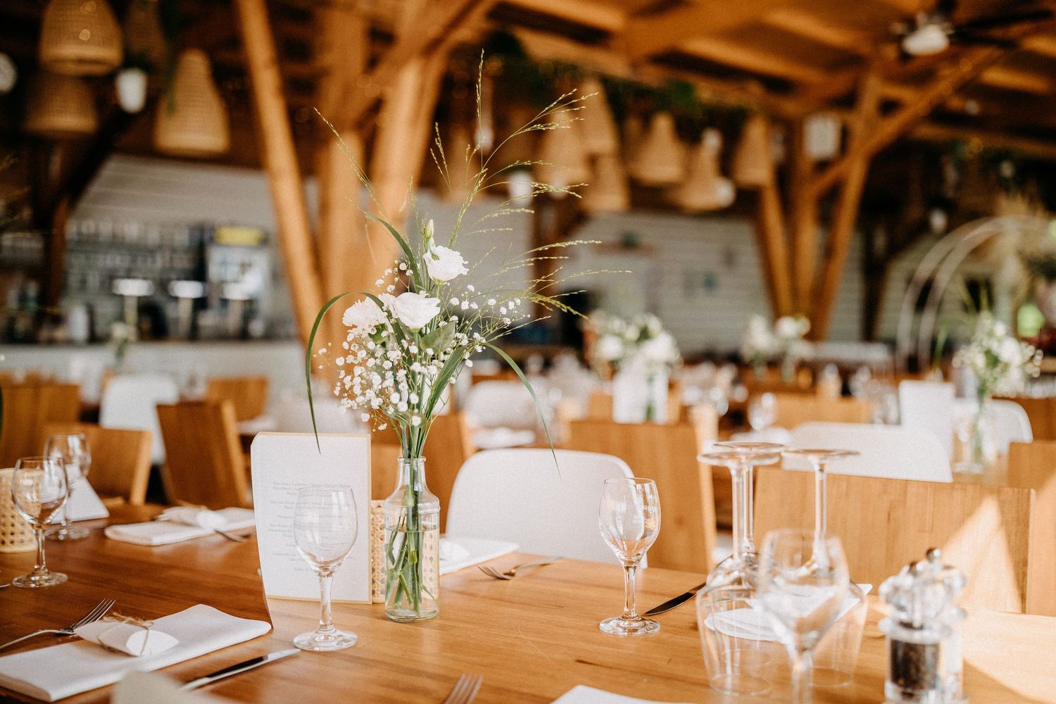 Rustikaler Hochzeitsempfangstisch mit Glasvasen mit zarten floralen Mittelstücken in einem Holzbalken.